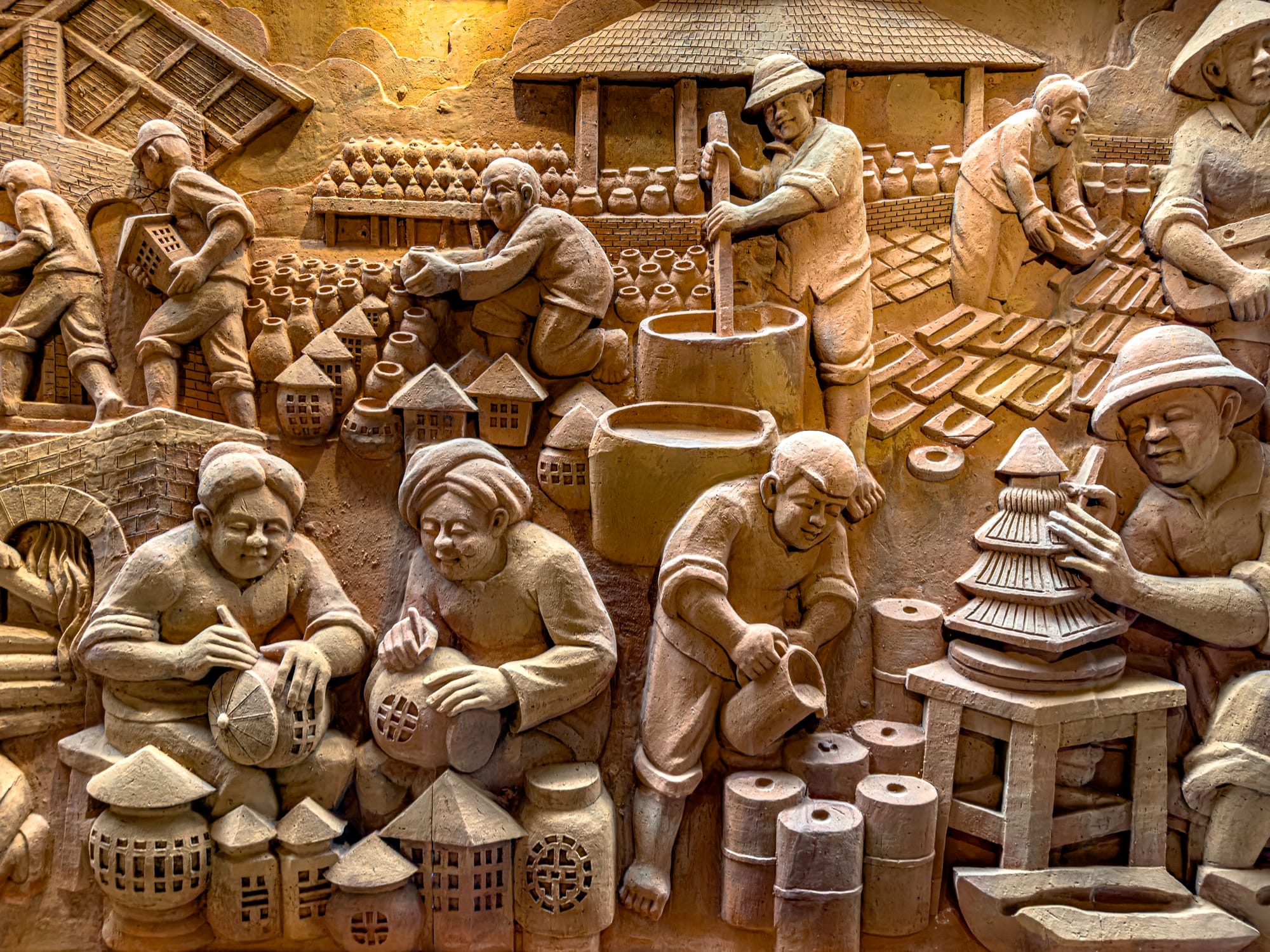 Clay bas-relief mural of Vietnamese artisans engaged in pottery making at the Terracotta Park in Thanh Hà Pottery Village Hội An, depicting traditional ceramic craft and village life