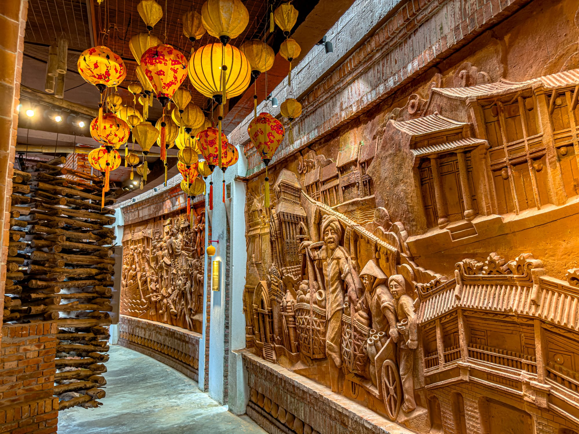 Clay bas-relief murals and traditional lanterns inside the Terracotta Park at Thanh Hà Pottery Village Hội An, depicting Vietnamese daily life scenes in ceramics