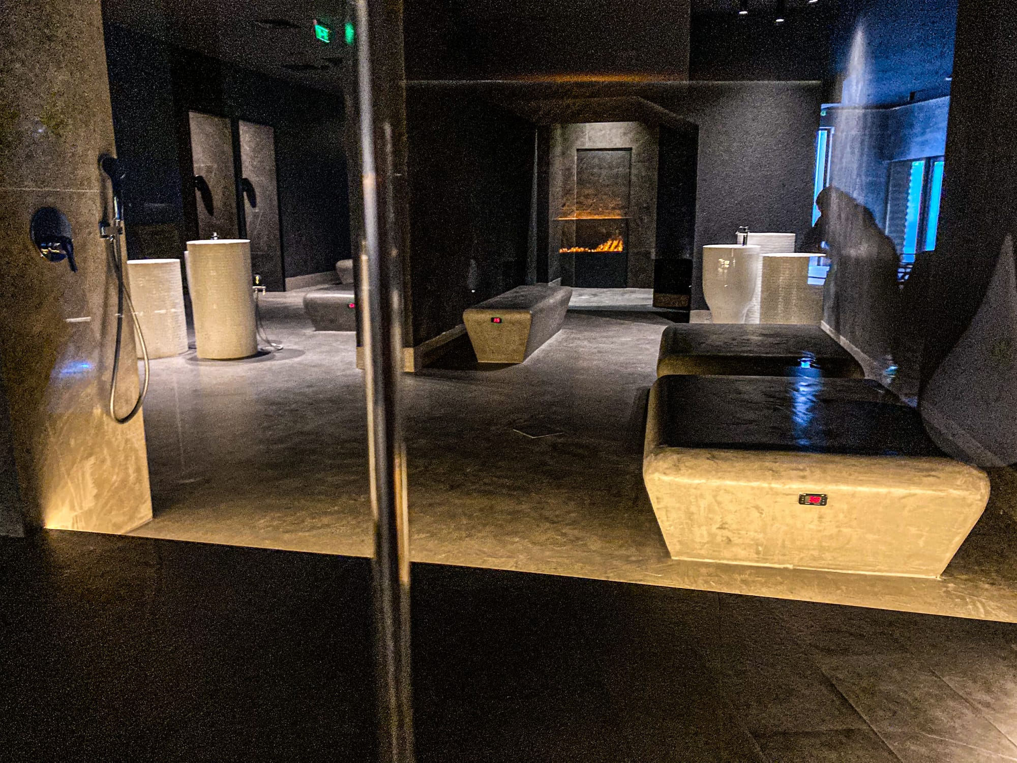 Dimly lit private treatment room at Pulse Thermal Spa in Banya, Bulgaria, with heated stone loungers, basins, and a wall-mounted fireplace