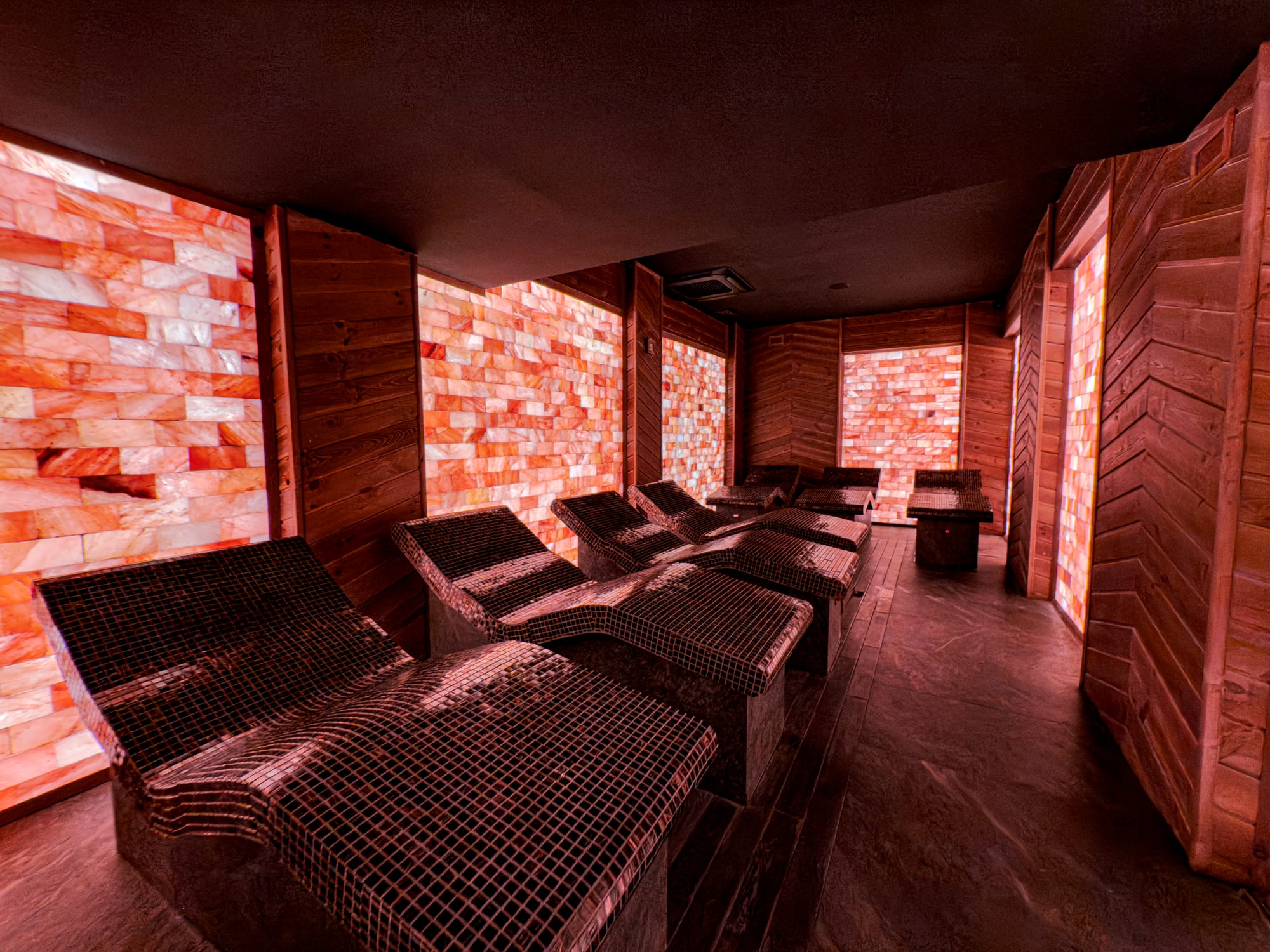 Row of heated tiled loungers inside the Himalayan salt room at Pulse Thermal Spa in Banya, Bulgaria, with glowing salt block walls and wood-paneled design