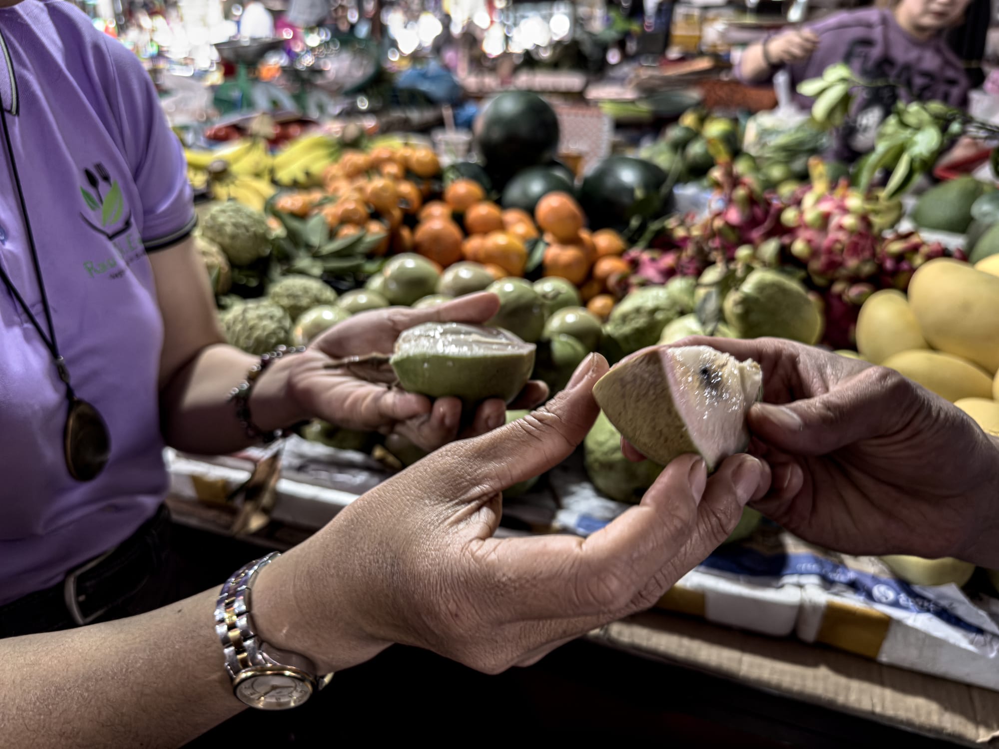 Hands holding sliced tropical fruit during tasting at Tân An Market produce stalls in Hội An, Vietnam