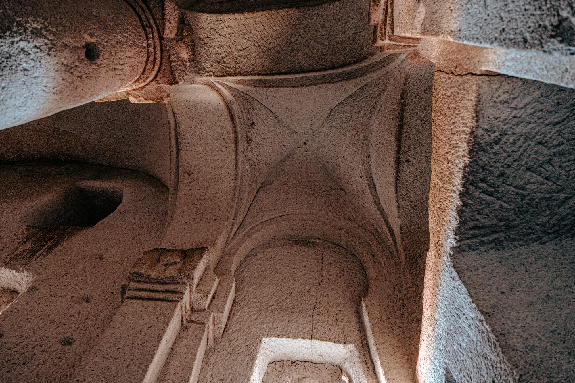Detailed view of the carved stone vaulting and arched ceiling inside the Column Church in Cappadocia, showing the smooth curves, intersecting arches, and natural light illuminating the textured rock surface