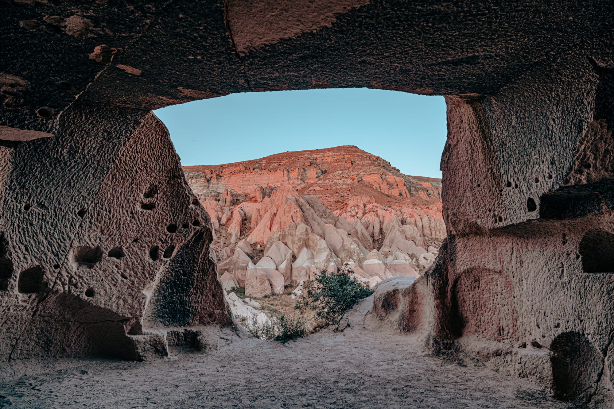 Framing Cappadocia’s rose-hued cliffs through the cool shade of an ancient cave