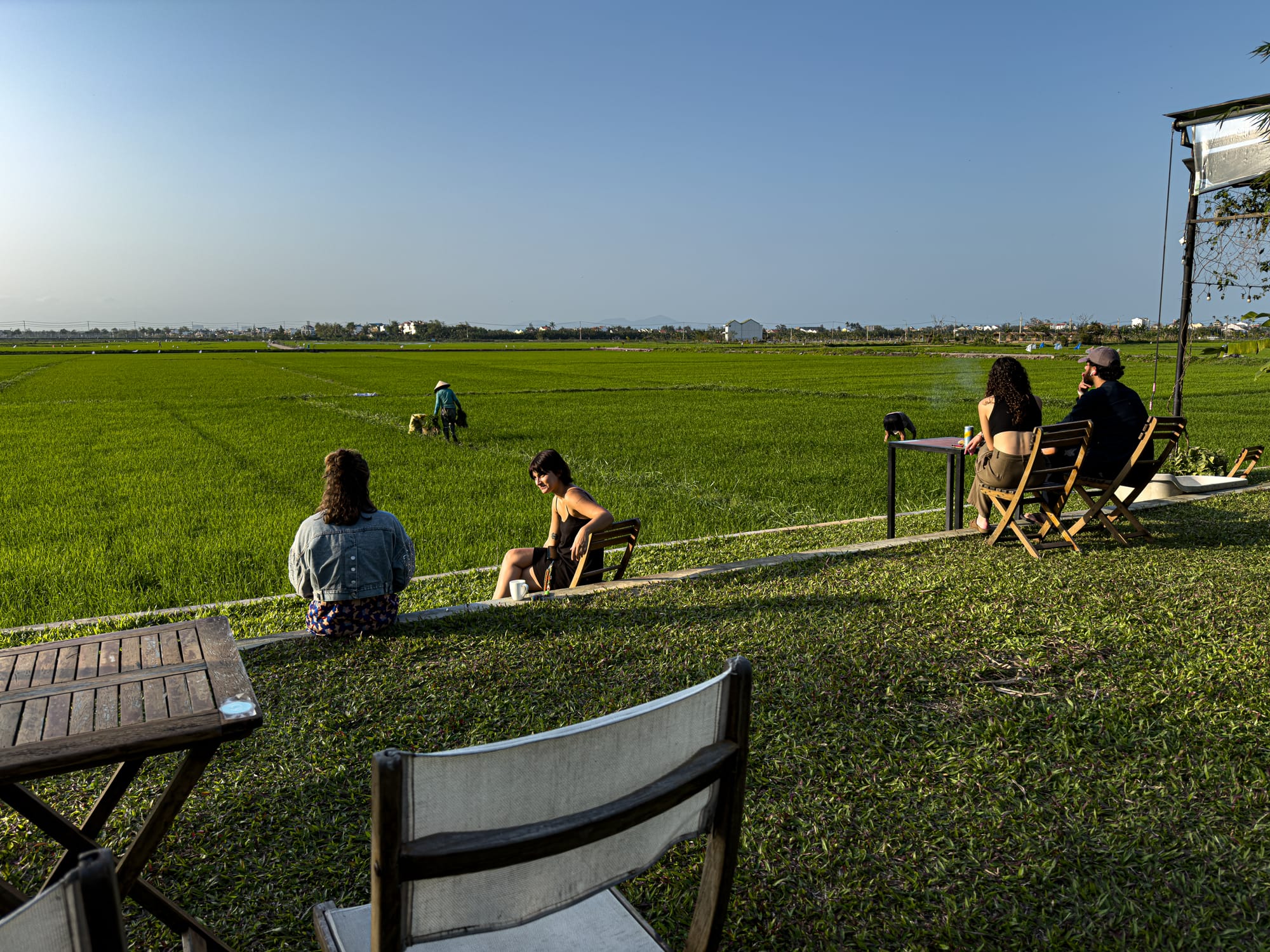 People sitting at outdoor tables overlooking the green rice fields at Hub Hoi An coworking space, surrounded by Vietnam’s peaceful countryside