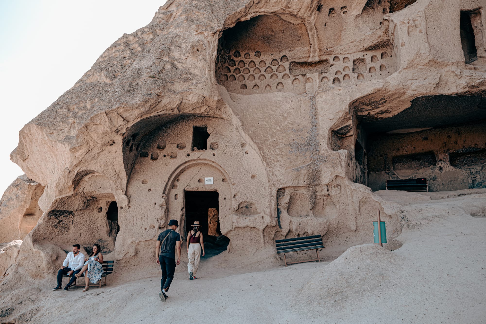 Visitors walking into a rock-carved entrance at Selime Monastery in Cappadocia with arched doorway and surrounding stone benches
