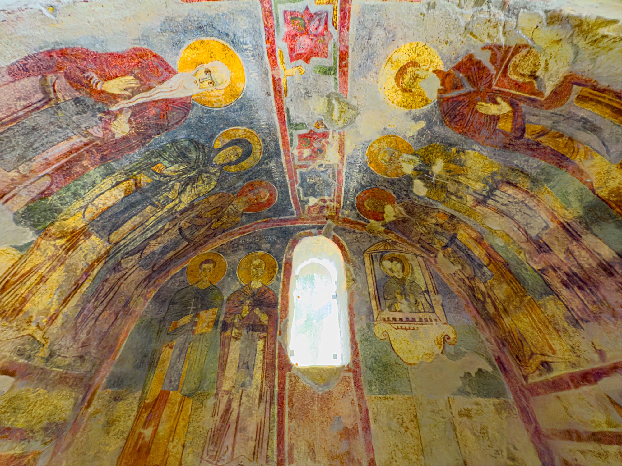 Byzantine frescoes with golden halos and biblical figures covering a curved ceiling above a narrow arched window in the Church of Saint Nicholas in Demre, Turkey