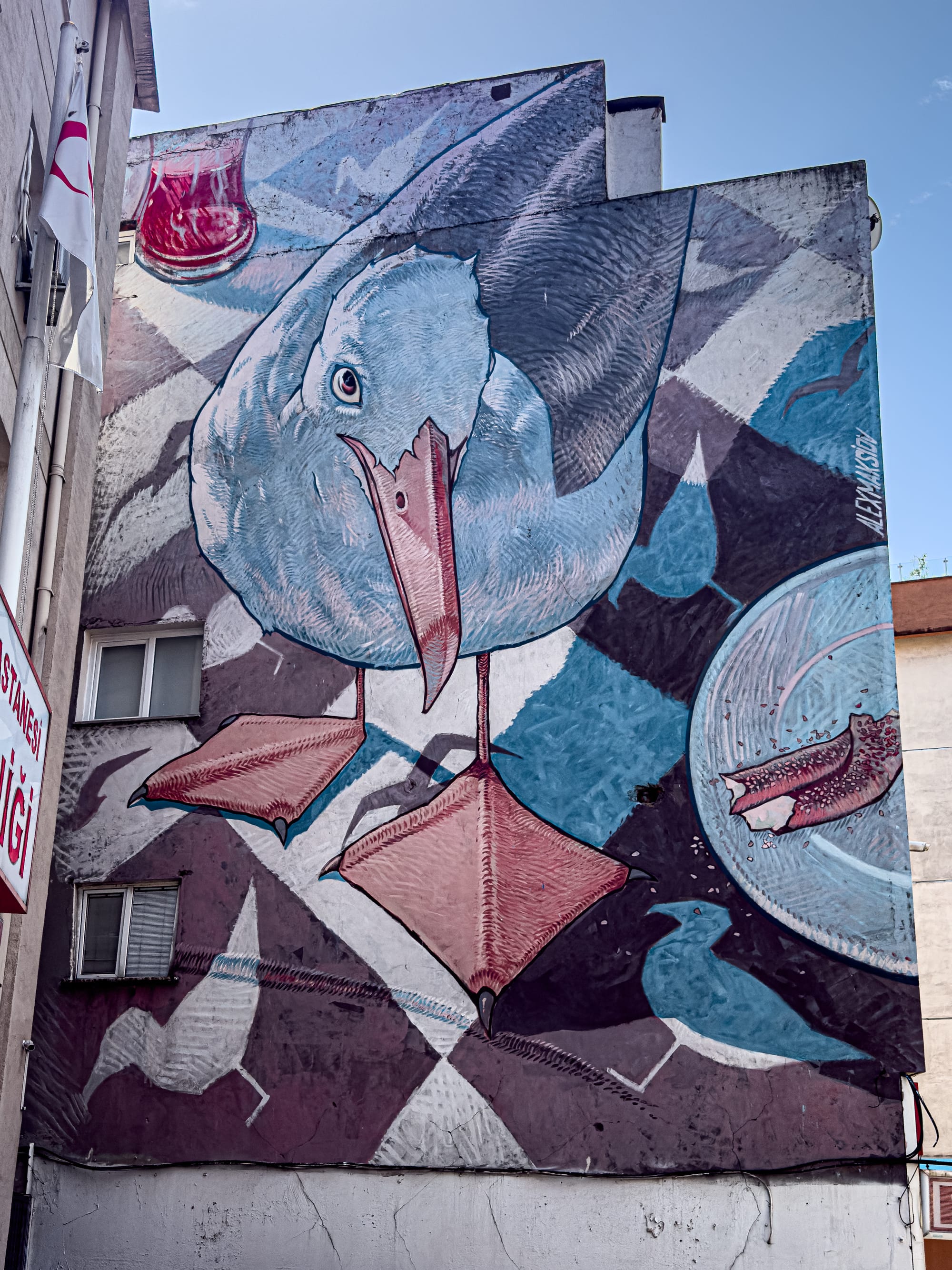 Mural of a blue-toned seagull with exaggerated feet and beak, set against a backdrop of Turkish tea glass, bread crusts, and abstract geometric patterns