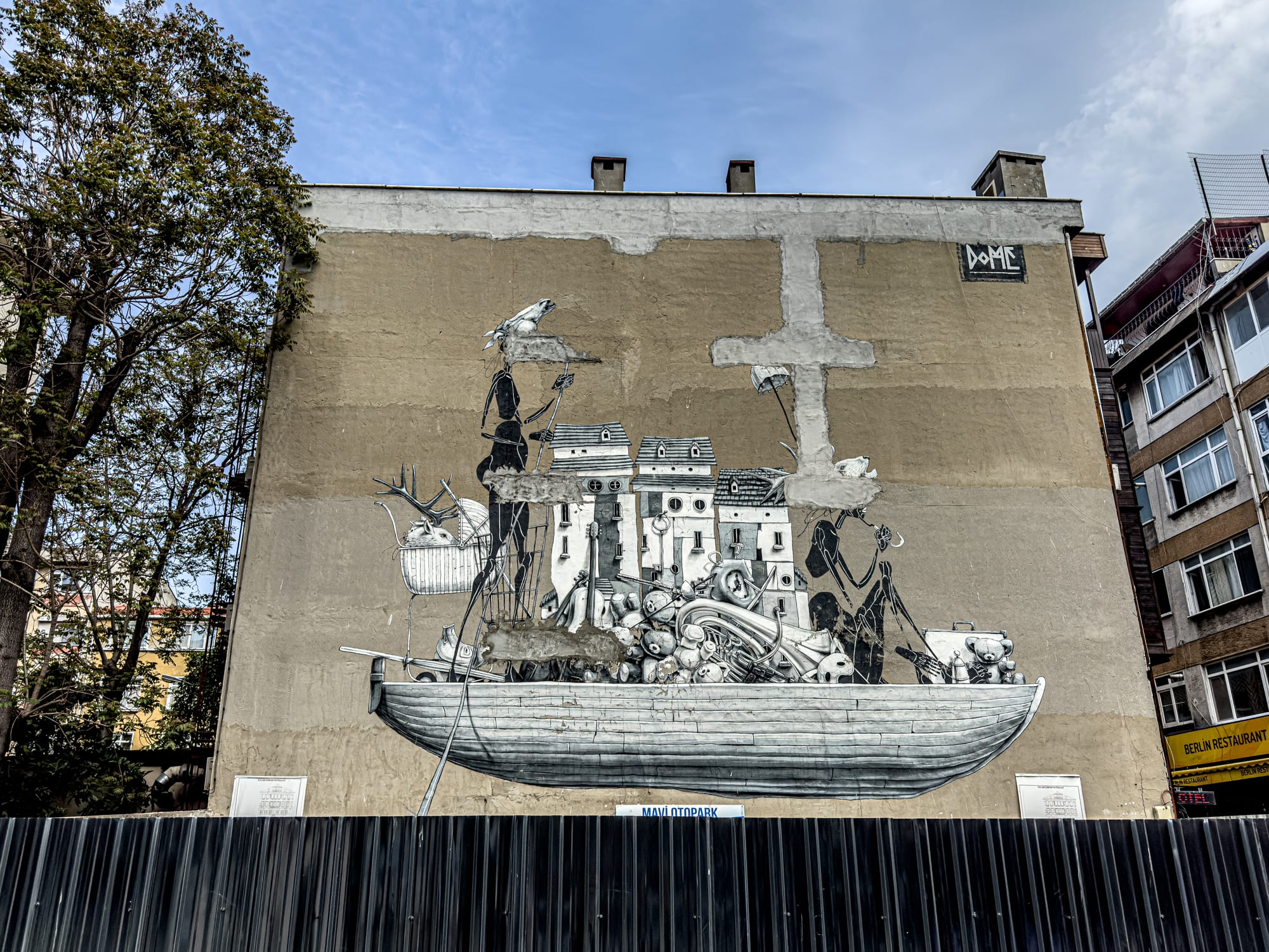 Black and white mural by Dome shows a surreal boat filled with tangled objects, buildings, and elongated human figures against a tan wall; above the vessel, fragmented forms and floating birds contribute to the dreamlike composition