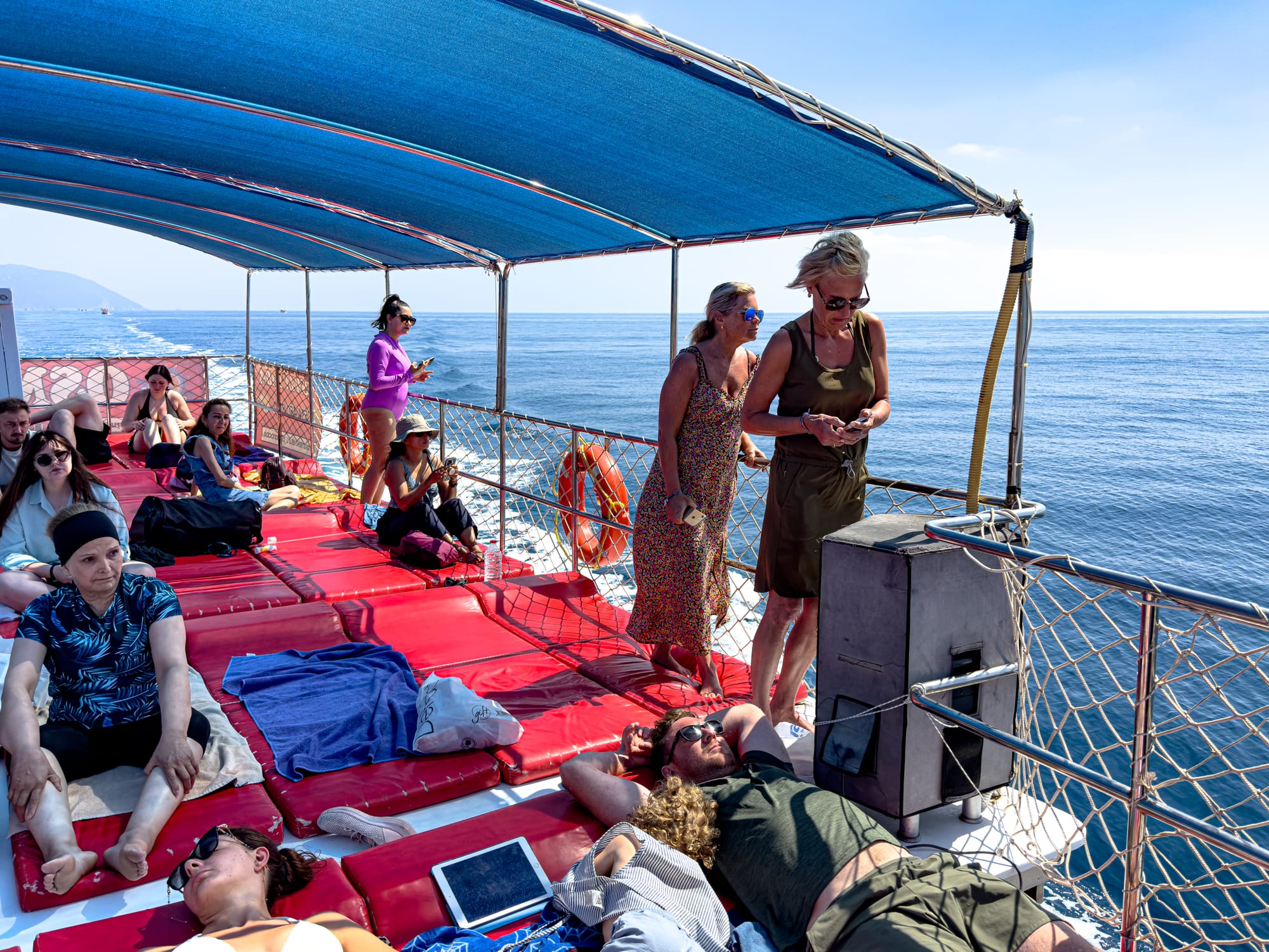 Travelers relaxing on cushioned mats under a shaded canopy on a boat’s upper deck, cruising through calm blue water toward Suluada