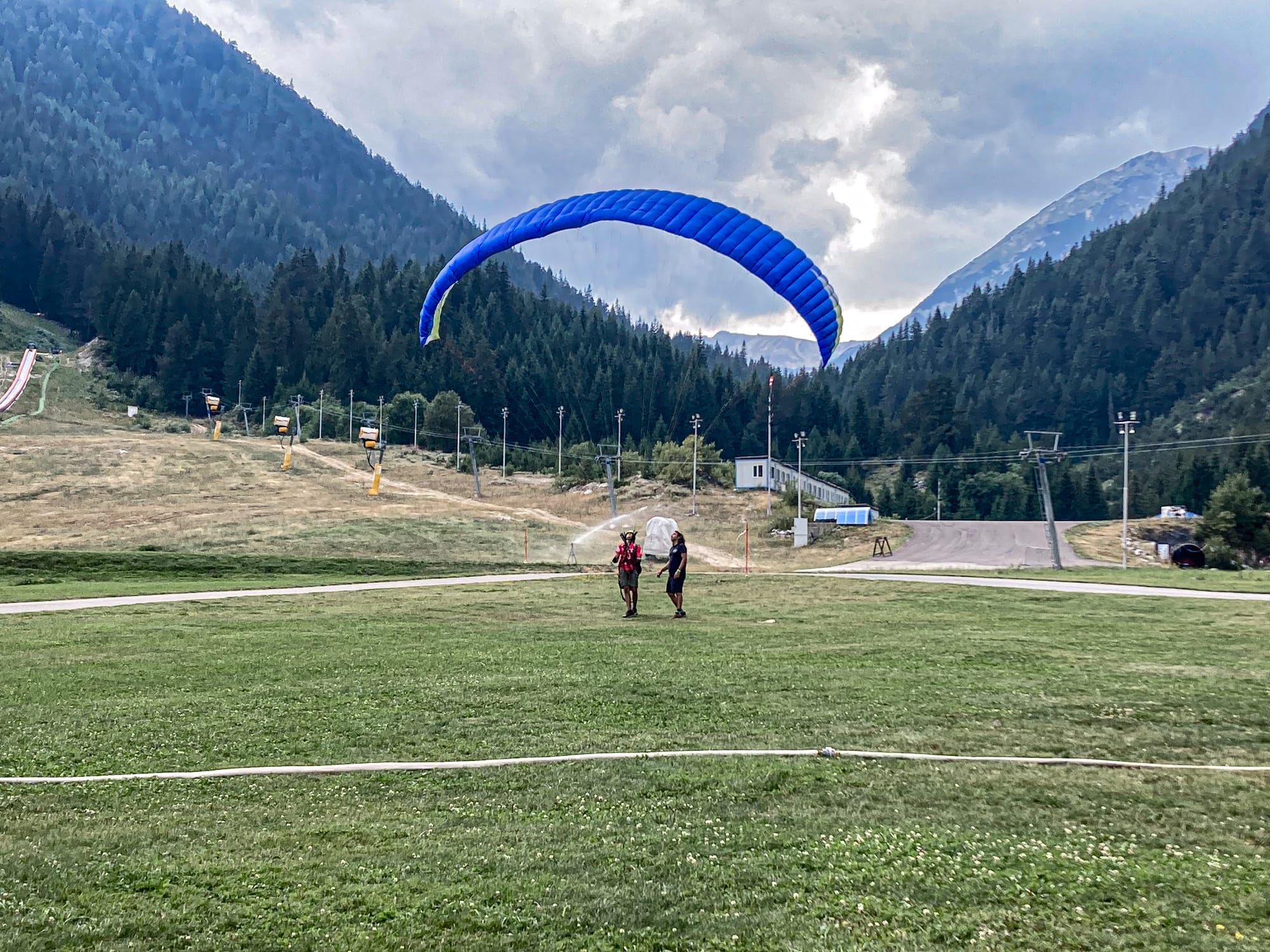 Person paragliding with a bright blue canopy against the mountain backdrop of Bansko, Bulgaria