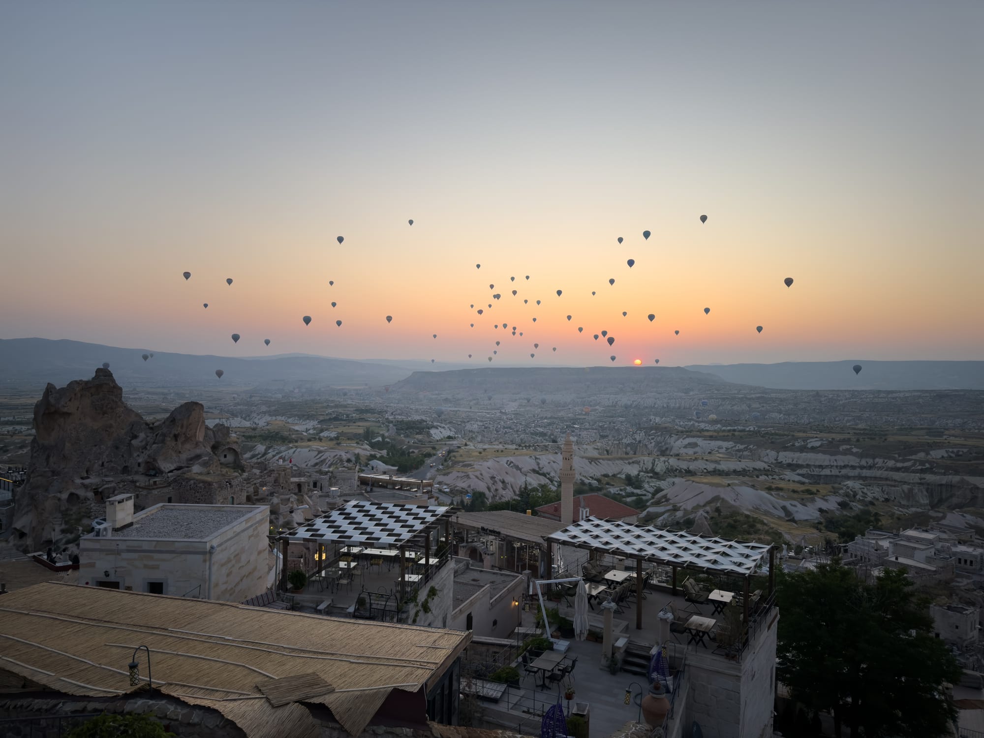 View from Uçhisar Castle at dawn in Cappadocia, Turkey: dozens of colorful hot air balloons rising over the sculpted ridges and rock valleys
