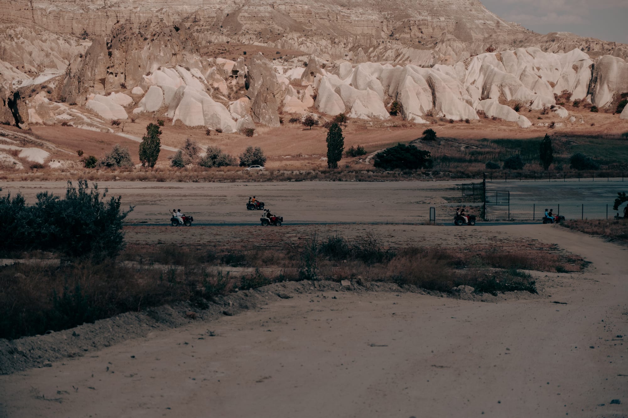ATV riders driving across a wide plain in Cappadocia with dramatic white rock formations rising in the background