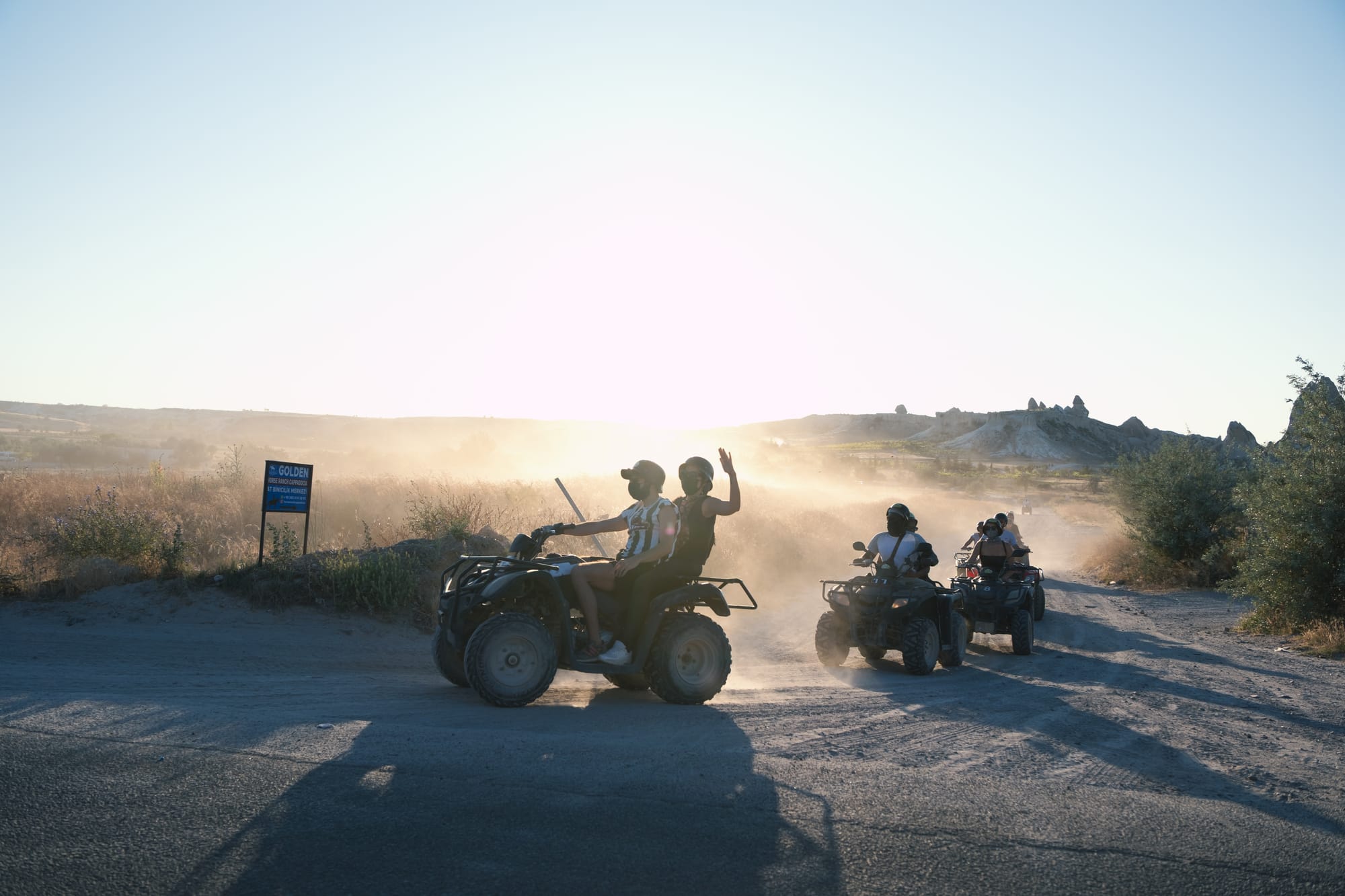 Group of ATV riders driving on a dusty trail in Cappadocia at sunset, with golden light shining through the haze