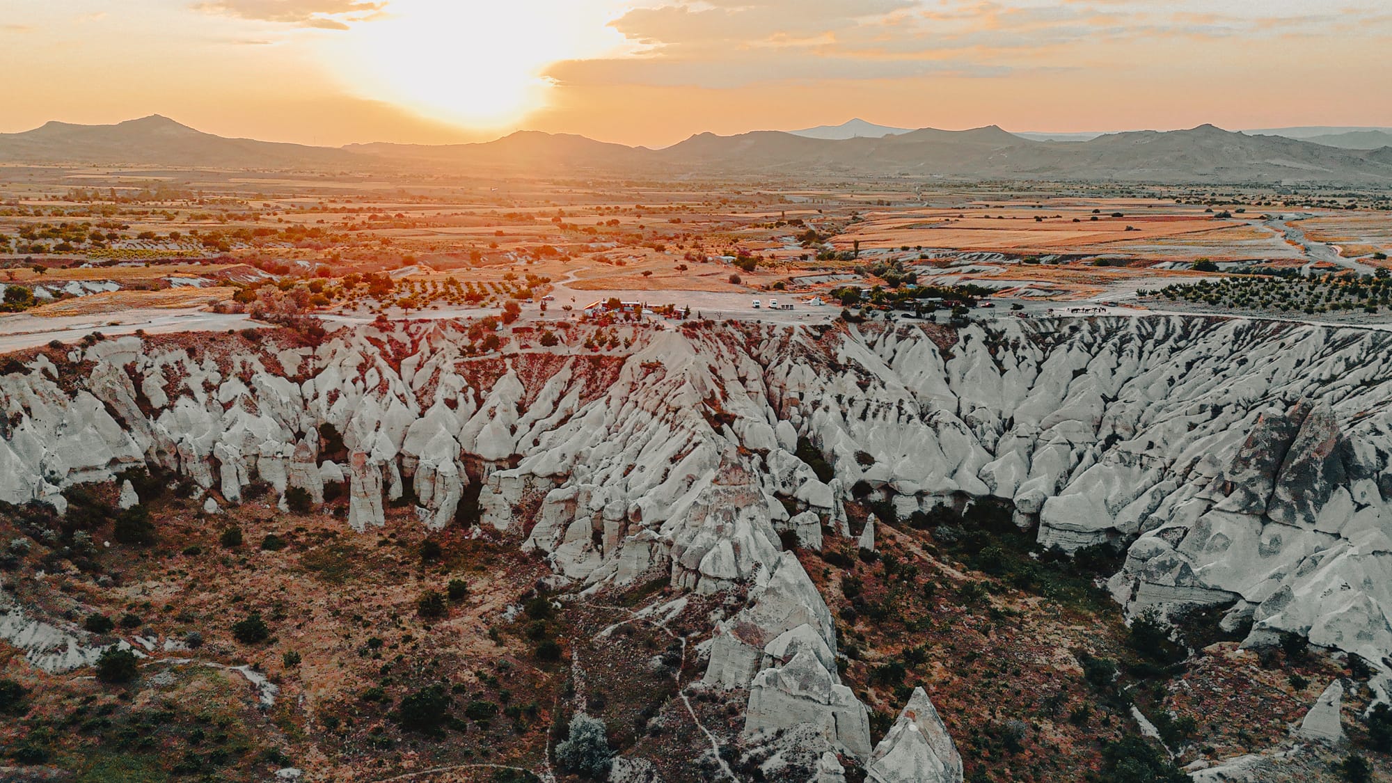 Sunset view of Love Valley in Cappadocia with white rock formations in the foreground and the sun setting over distant mountains
