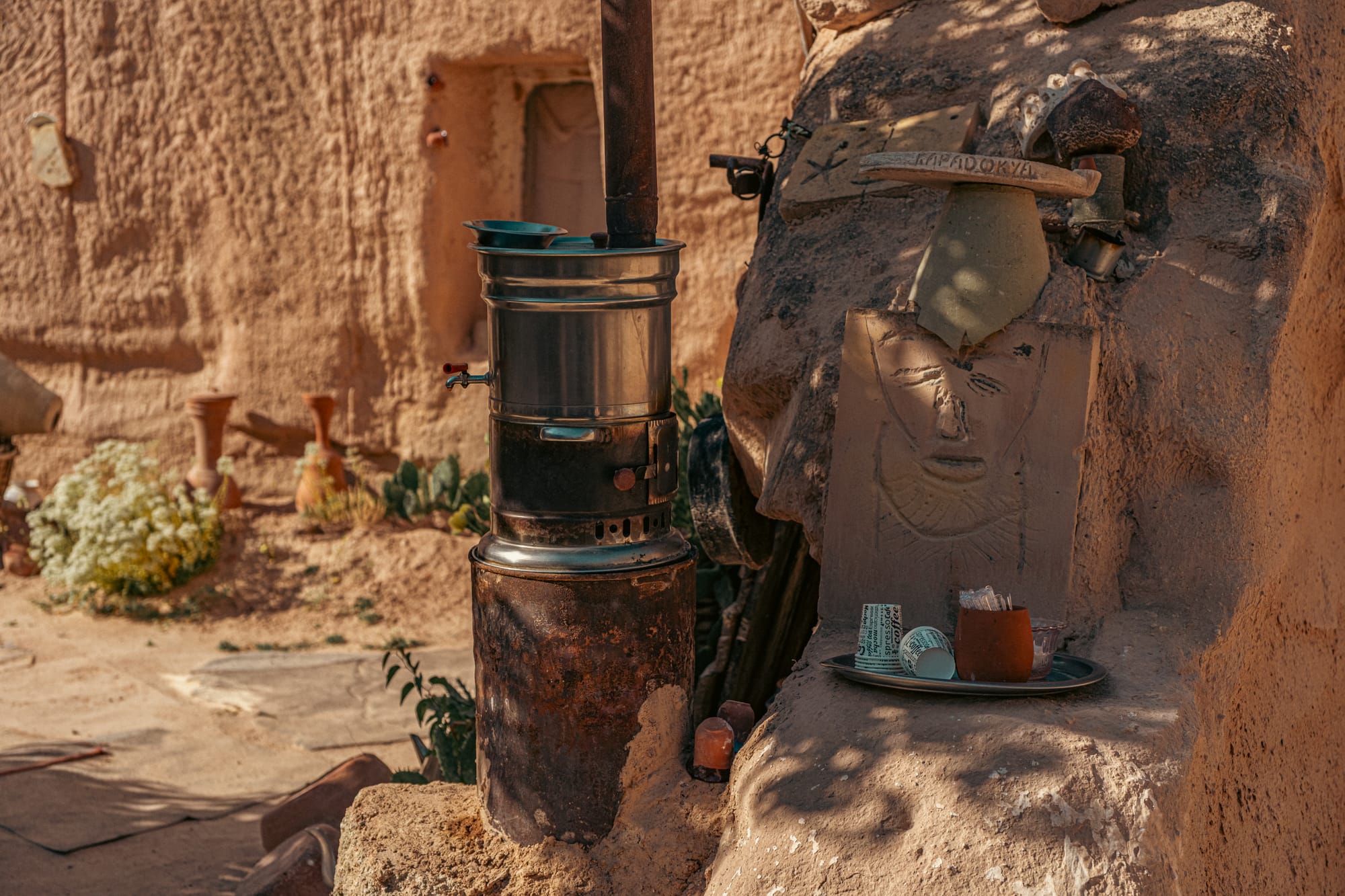 Metal samovar for brewing tea placed on a stone base in the courtyard of Tarihi Ev Historical House in Çavuşin, Cappadocia, with terracotta pottery, carved stone artwork, and desert plants in the background