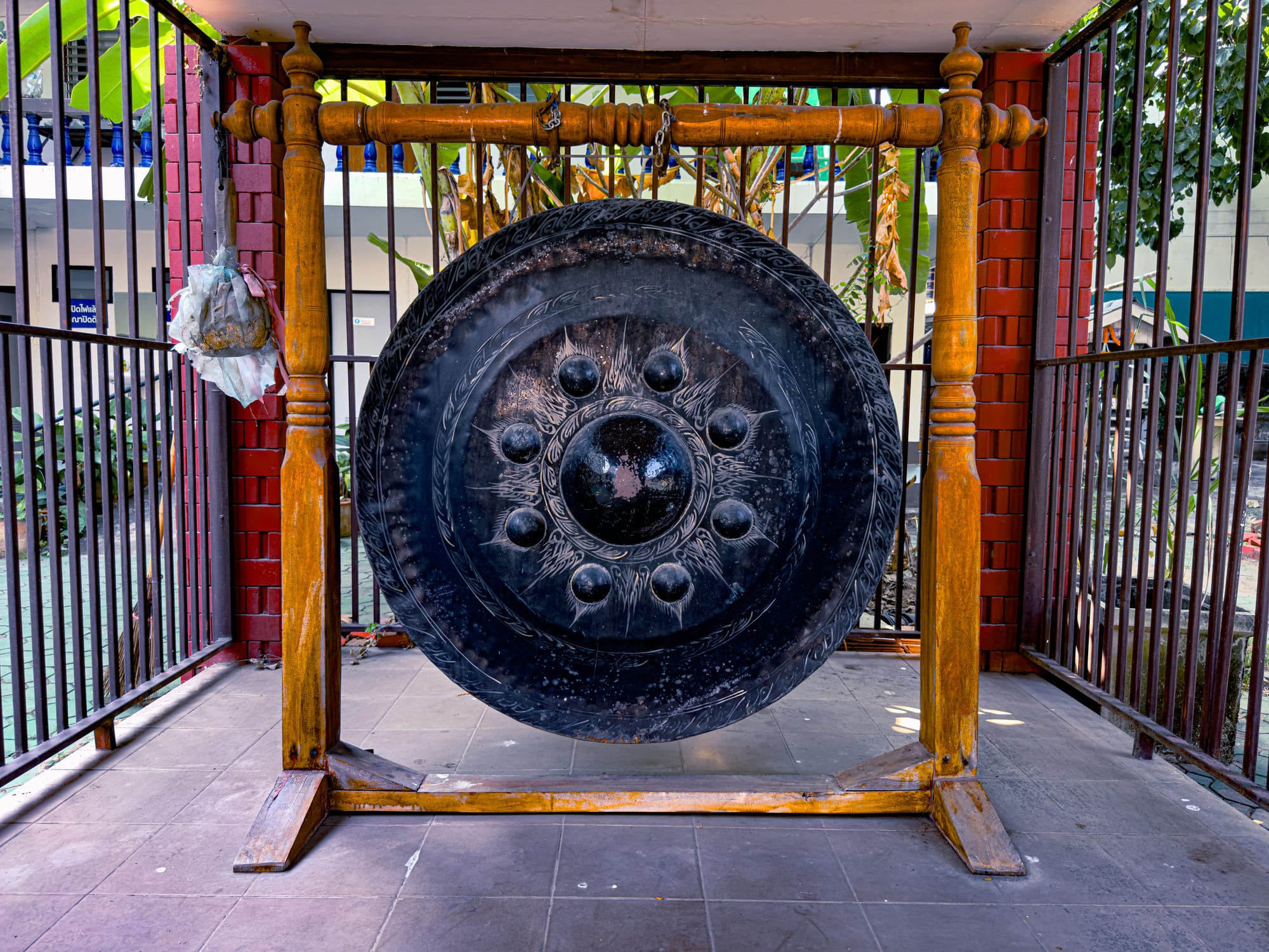 A black ceremonial gong with ornate carvings, suspended in a wooden frame, placed within a temple courtyard in Chiang Mai