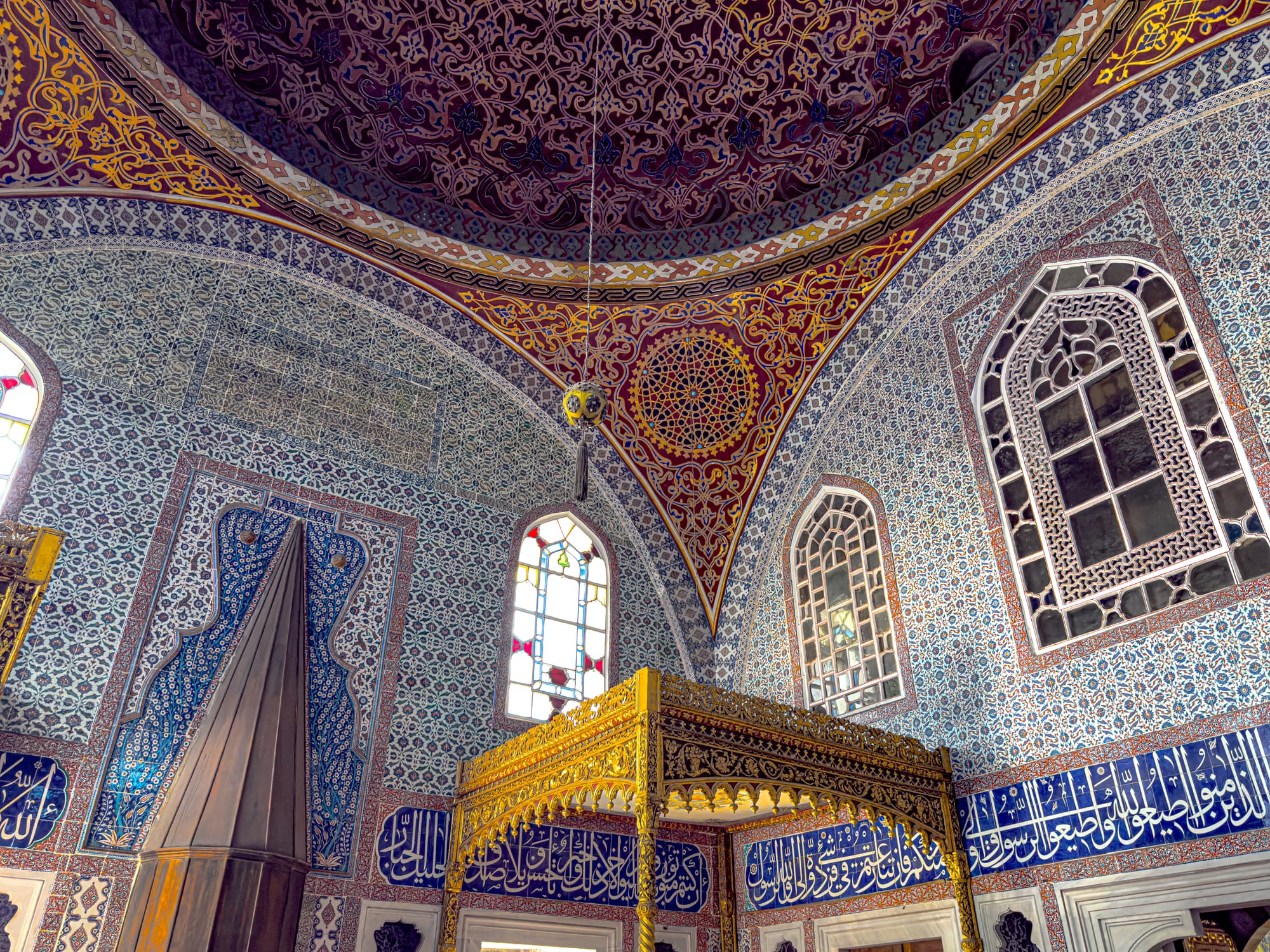 Interior of Topkapi Palace with intricate Iznik tilework, stained glass windows, and an ornate dome ceiling