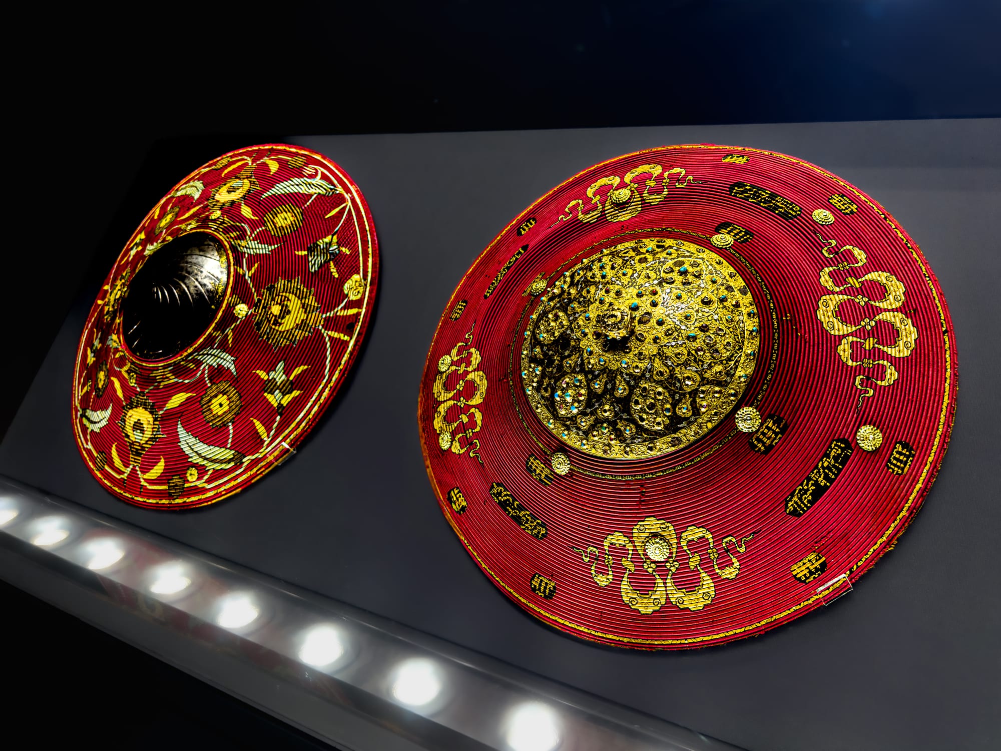 Two ornate Ottoman shields on display, decorated with red lacquer, gold filigree, and precious stones