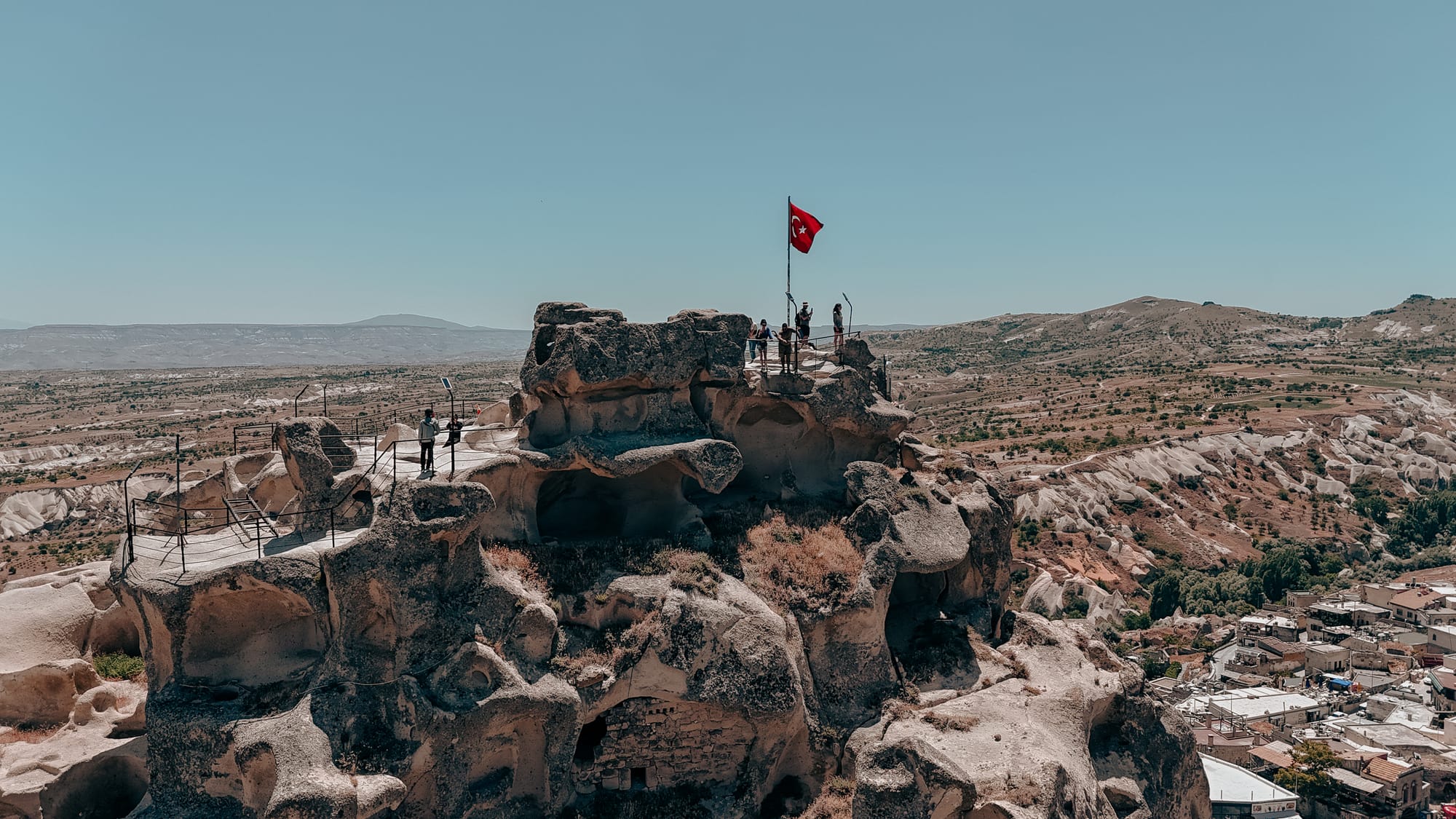Uçhisar Castle Cappadocia summit with Turkish flag and visitors overlooking valleys and rock formations