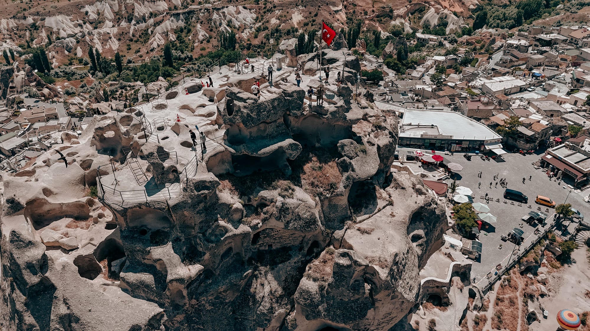 Uçhisar Castle Cappadocia summit aerial view with Turkish flag, visitors, and panoramic town below