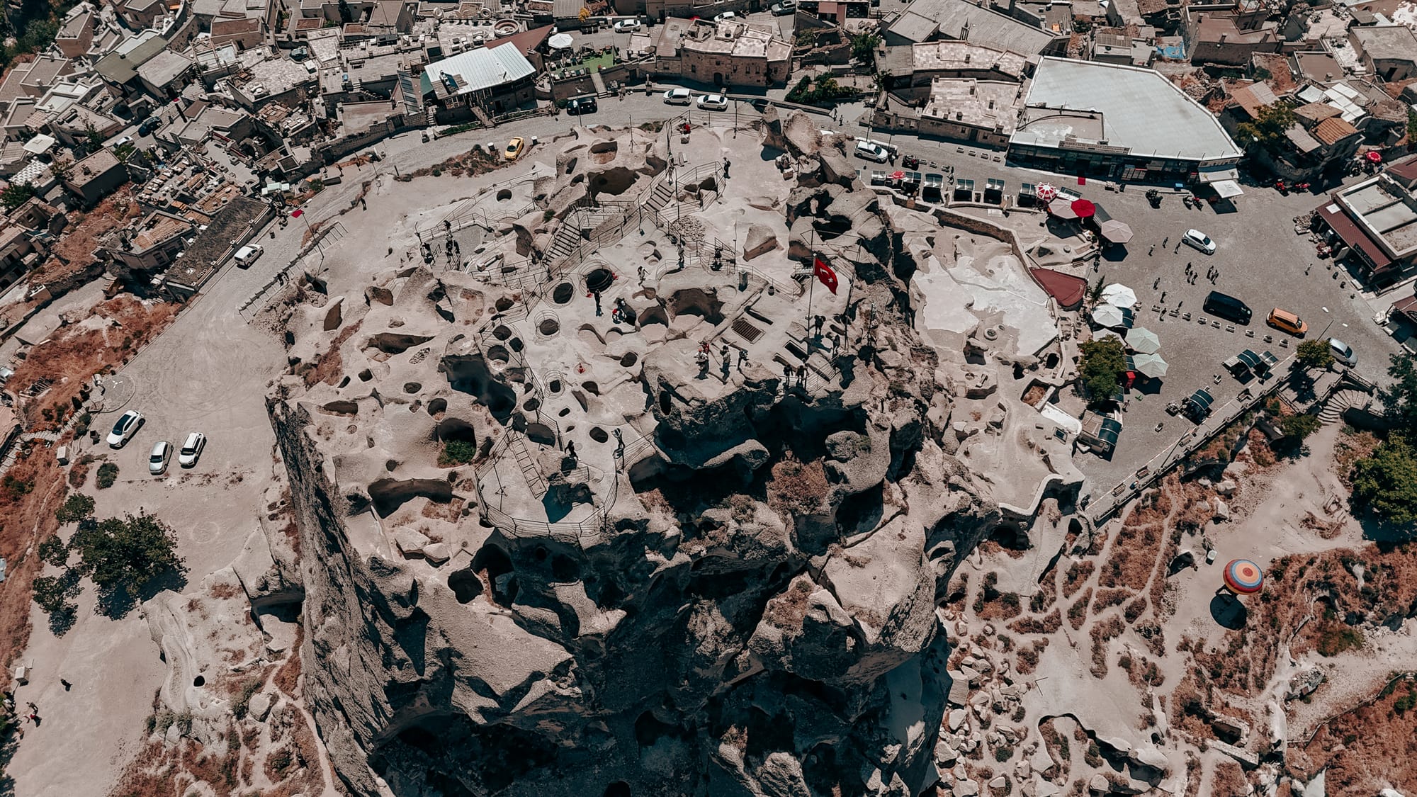 Uçhisar Castle Cappadocia aerial view showing summit with Turkish flag, visitors, and panoramic town surroundings