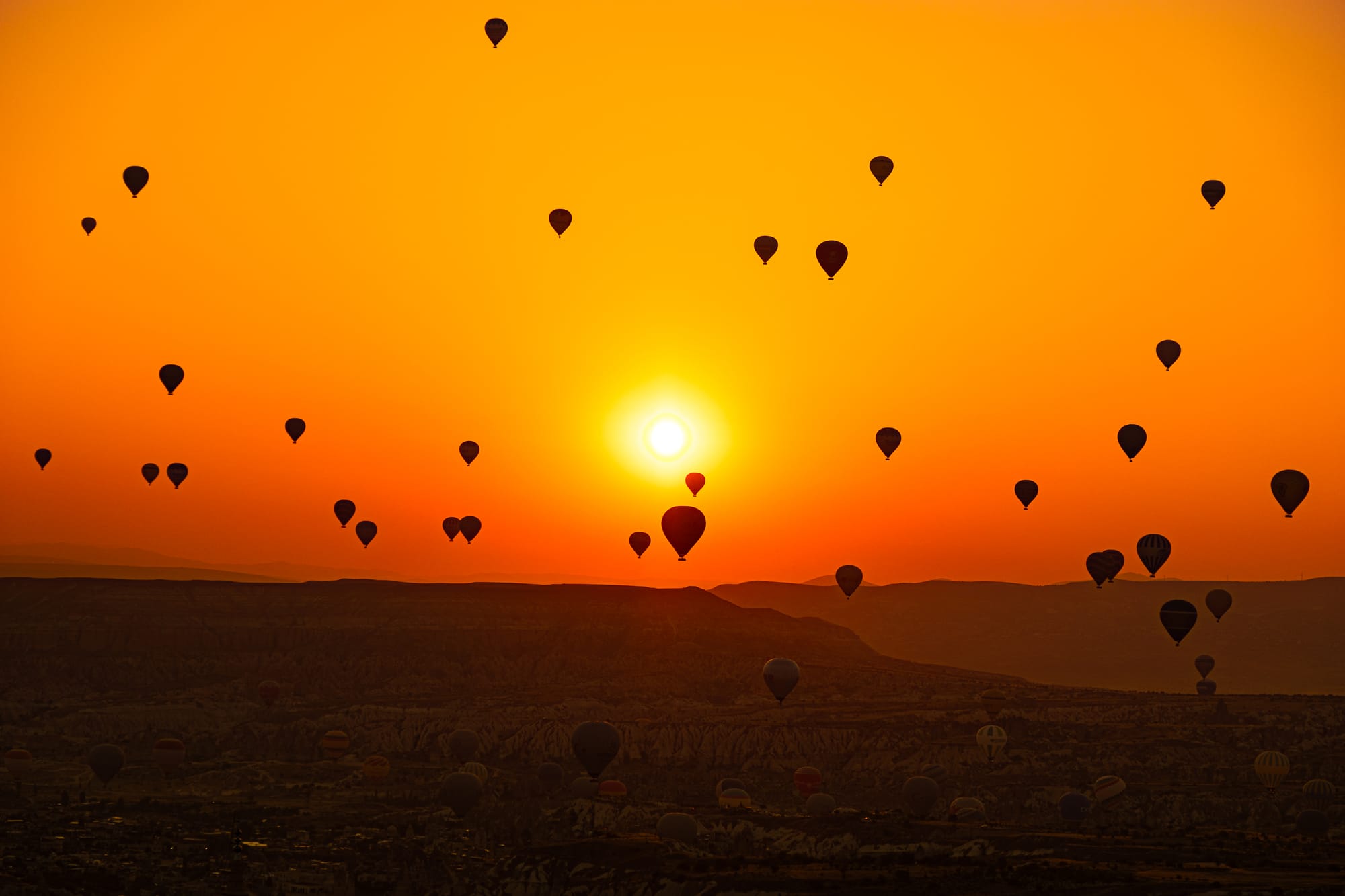 Uçhisar Castle Cappadocia sunrise view with dozens of hot air balloons floating above valleys