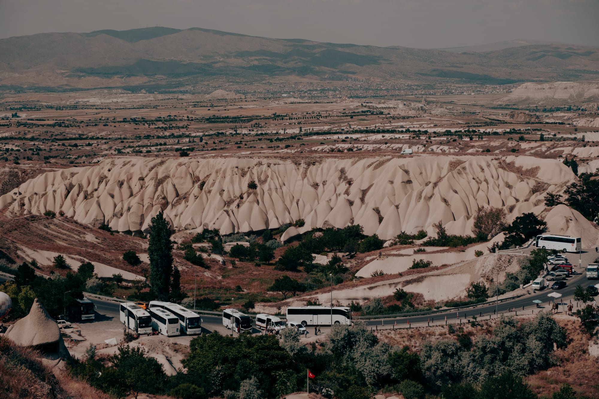 Uçhisar Castle Cappadocia valley view with unique eroded ridges, parked tour buses, and surrounding landscape near the walking trails