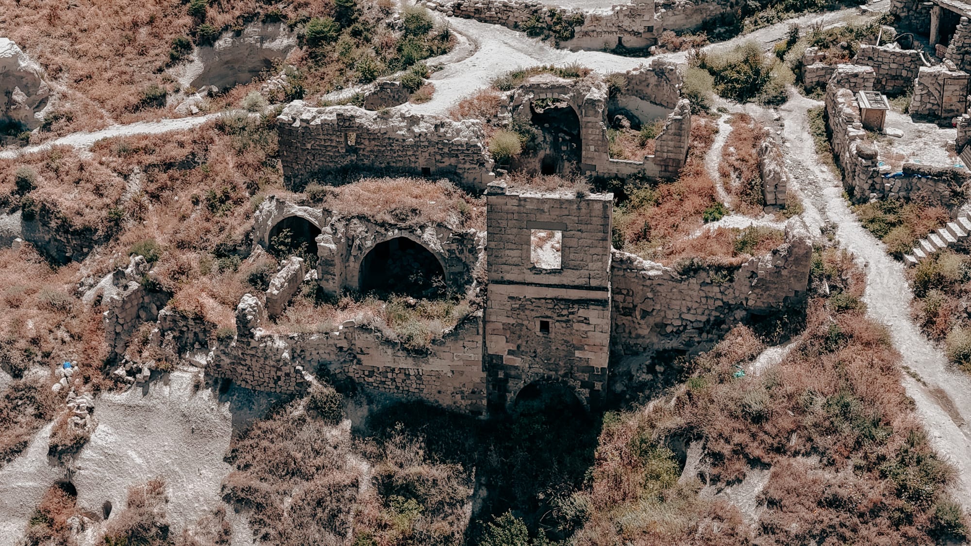 Uçhisar Castle Cappadocia ruins view showing old stone structures and overgrown paths along nearby walking trails