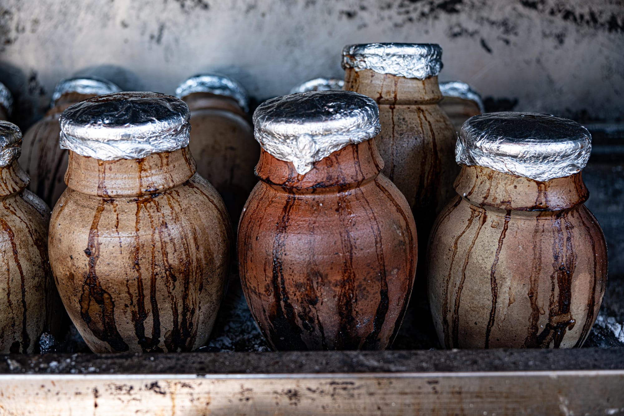 Foil-sealed clay pots streaked with cooking juices sit nestled in a charcoal oven, slow-cooking a rich vegetable stew inside
