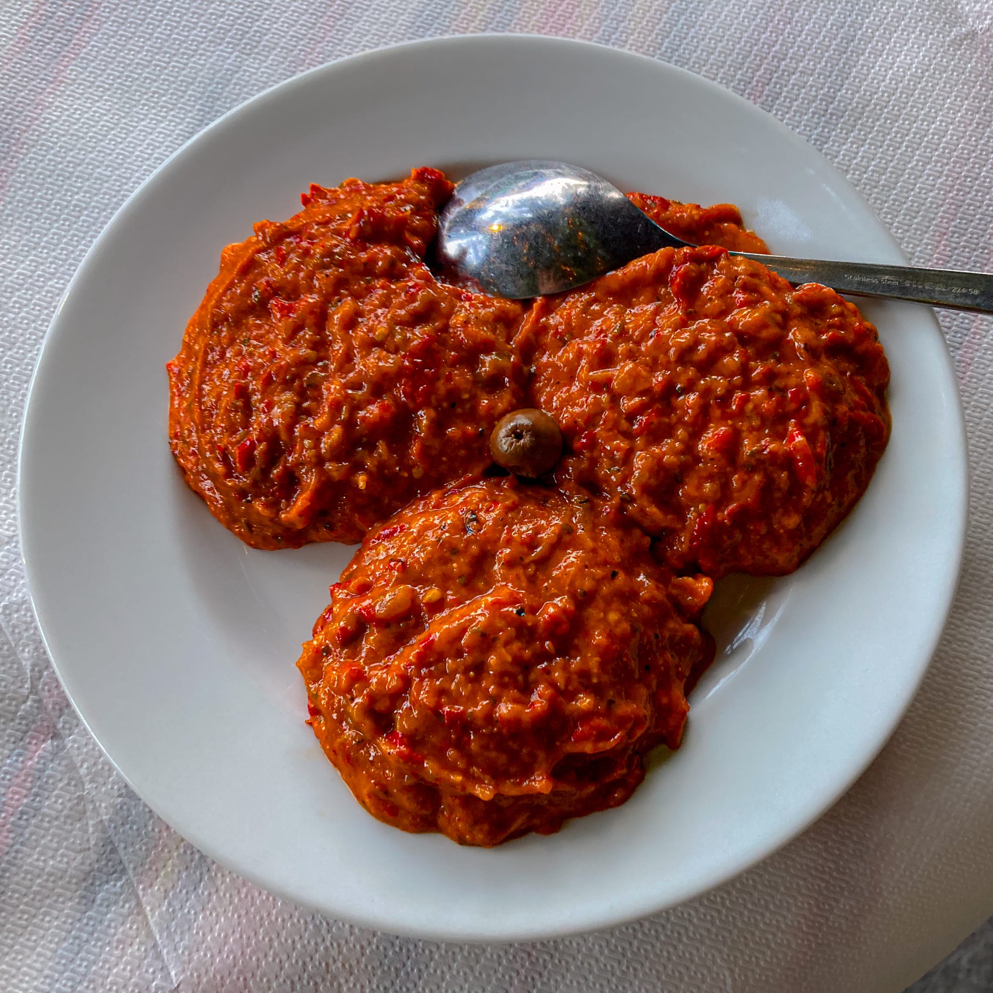 Plate of Bulgarian lutenitsa, a roasted red pepper and tomato spread, served in three scoops with an olive garnish and spoon on the side