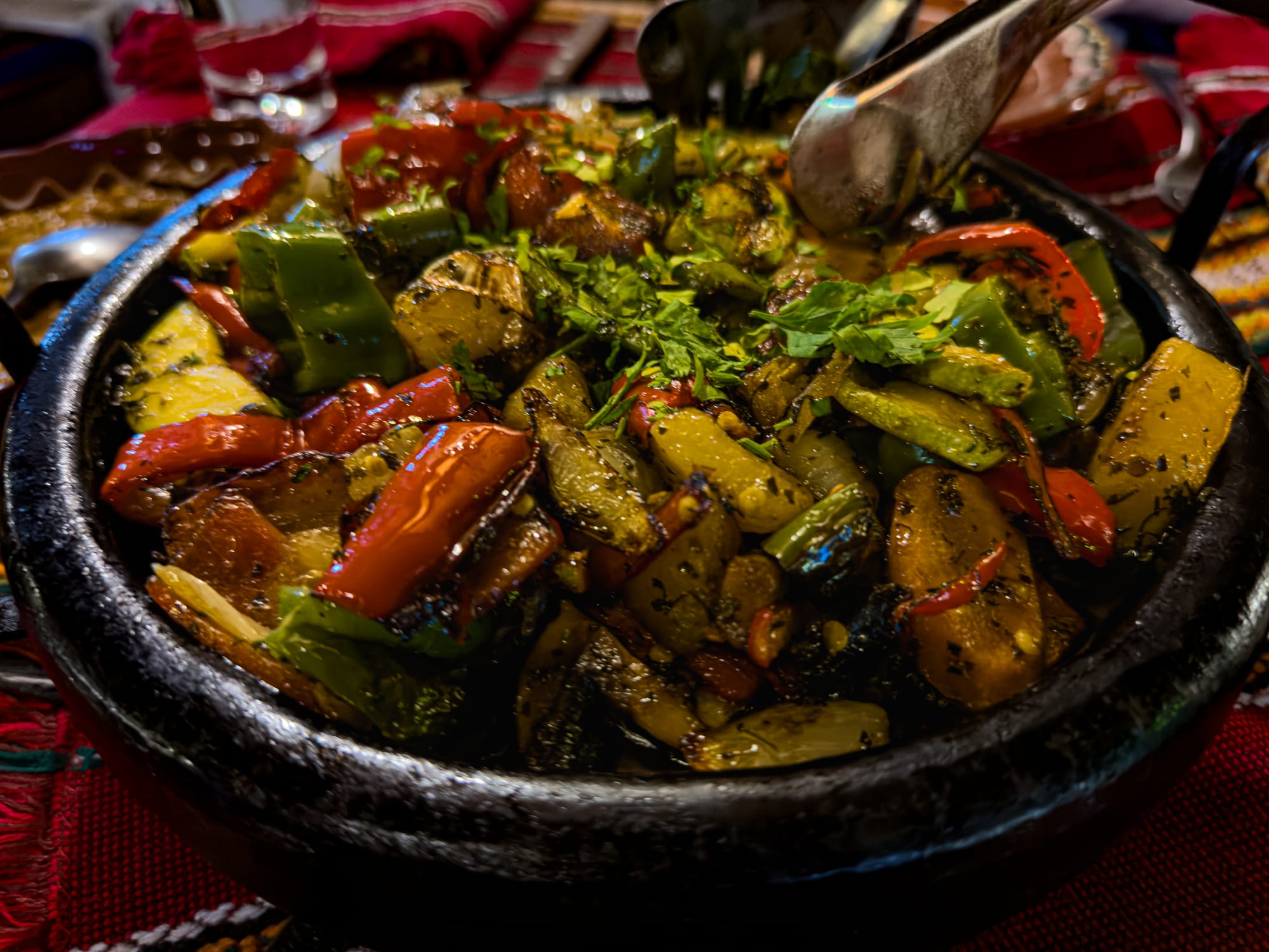 Close-up of a sizzling Bulgarian vegetable sach served in a black clay dish, filled with roasted peppers, zucchini, onions, and potatoes, garnished with fresh parsley