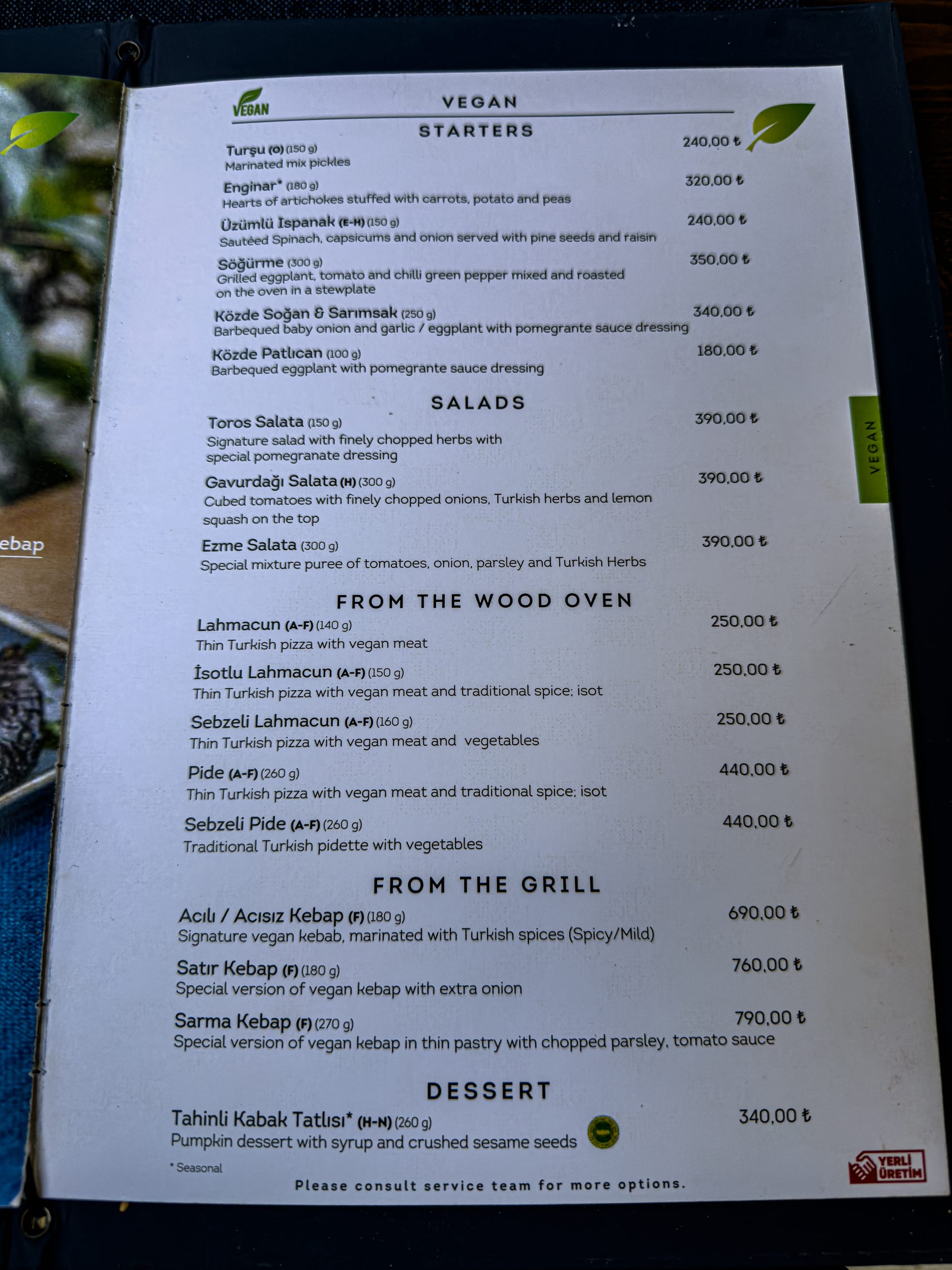 Photo of the vegan menu at Köşebaşı Kapadokya in Cappadocia, listing a variety of plant-based dishes including starters like grilled eggplant and artichokes, salads, vegan Turkish pizzas such as lahmacun and pide, vegan kebabs, and a pumpkin dessert with syrup and crushed sesame seeds, with prices in Turkish lira