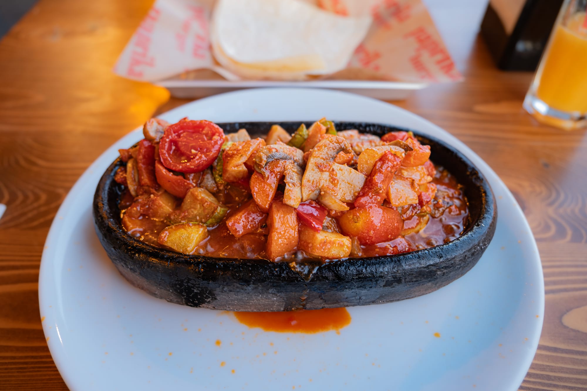 Close-up of a sizzling vegetable clay pot dish served at Paprika Burger & Pasta in Uçhisar, Cappadocia, featuring chunks of tomatoes, mushrooms, zucchini, carrots, and peppers in a rich red sauce, presented in a black stone serving dish on a white plate
