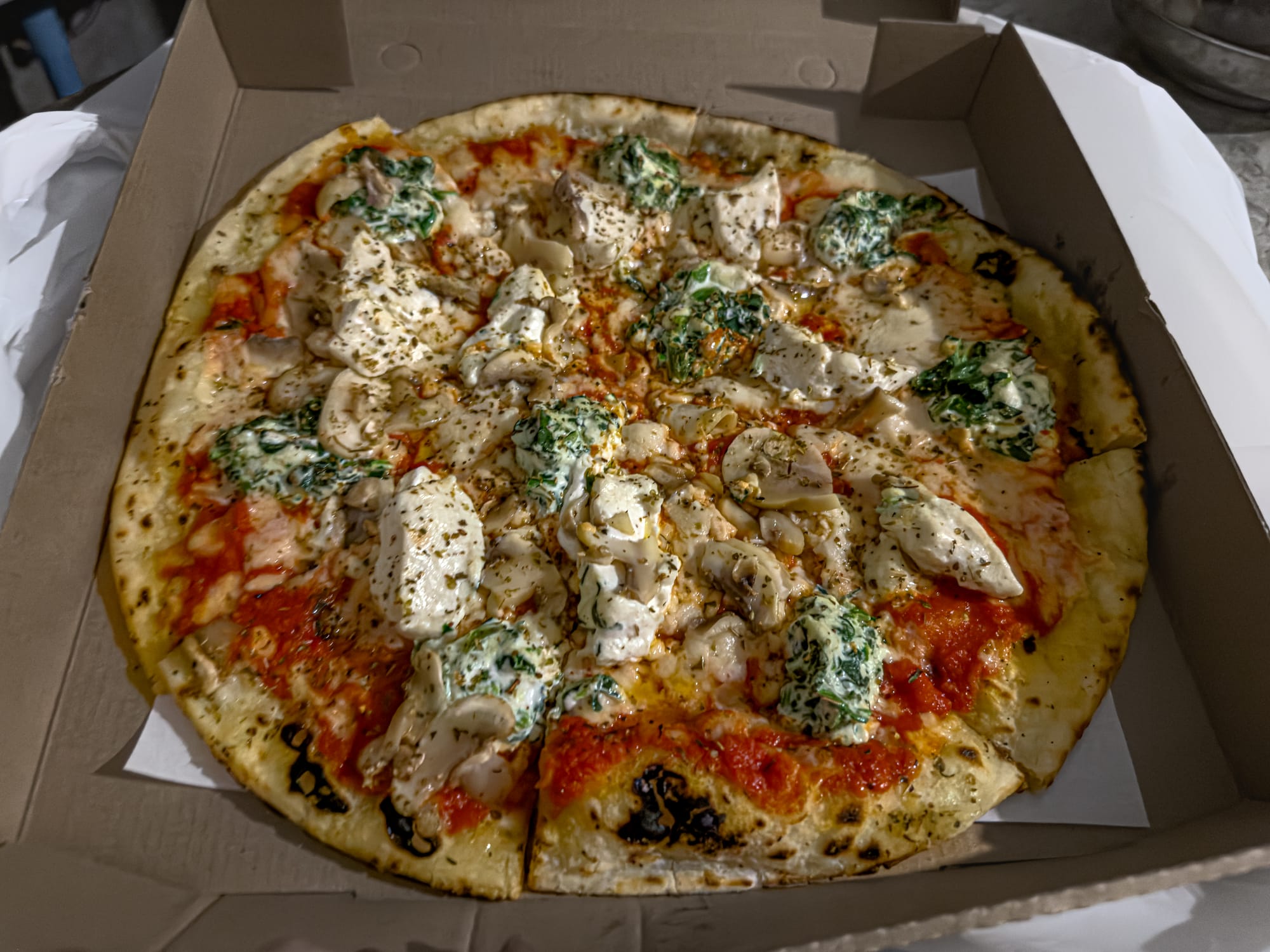 Vegan pizza in an open box from Goodsouls Kitchen in Chiang Mai, featuring a thin crust base layered with tomato sauce, mushrooms, herbs, and generous dollops of house-made cashew cheese