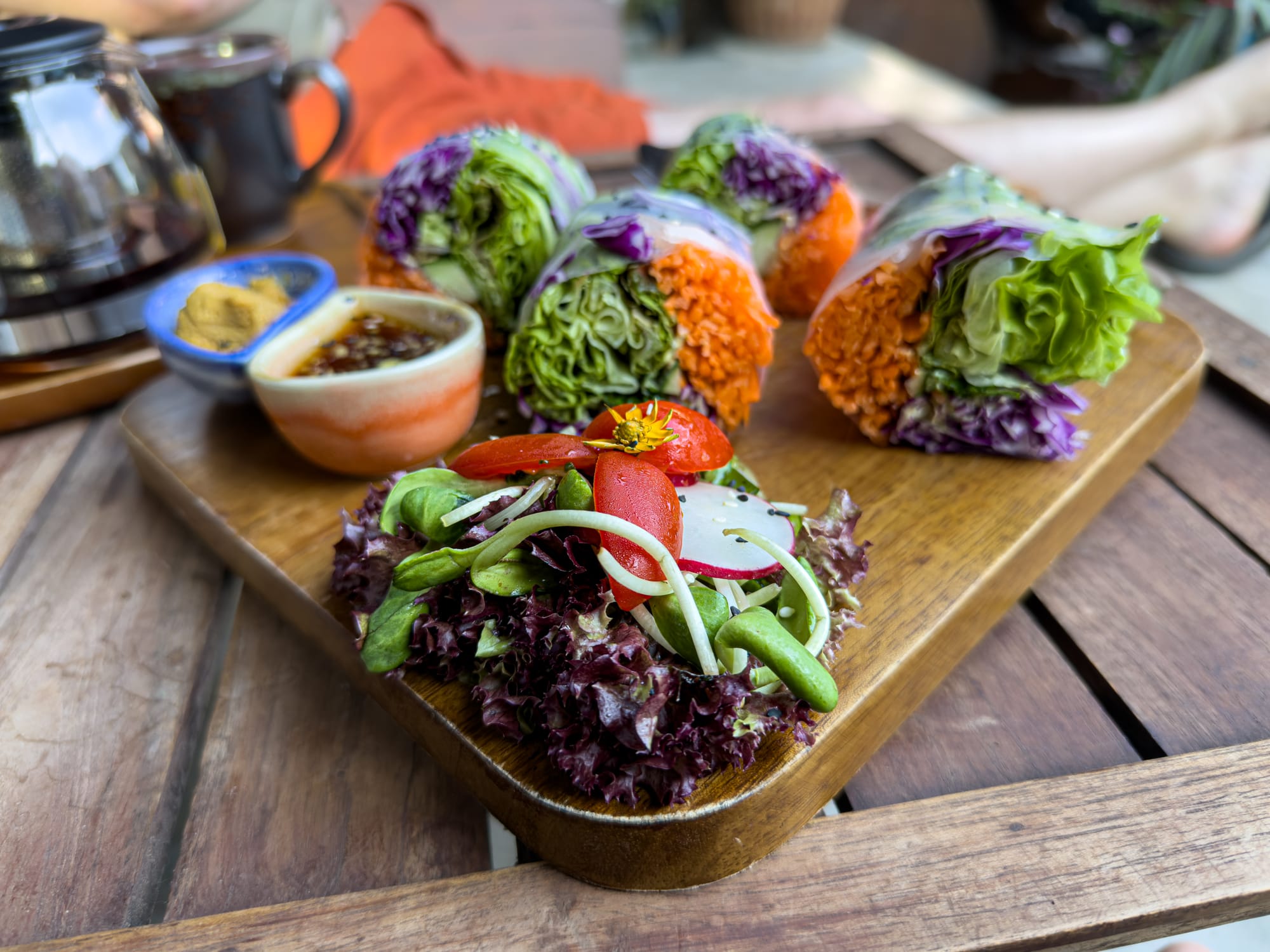 Close-up of vegan fresh spring rolls at Pure Vegan Heaven in Chiang Mai, filled with vibrant layers of lettuce, shredded carrots, and purple cabbage, served on a wooden board with a side salad, and dipping sauce