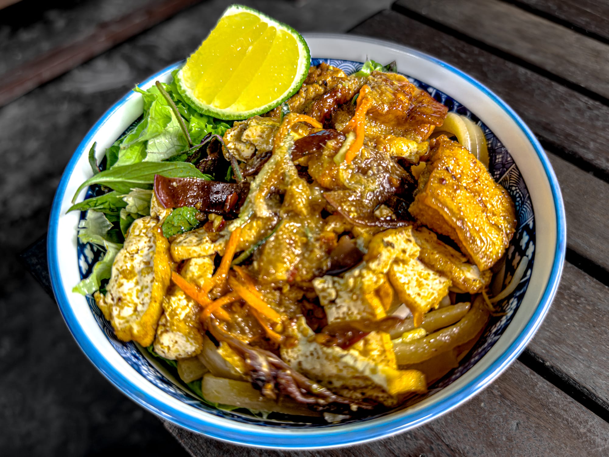 Vegan cao lầu noodle dish at Chickpea Eatery in Hội An with tofu, mushrooms, herbs, greens, and a lime wedge