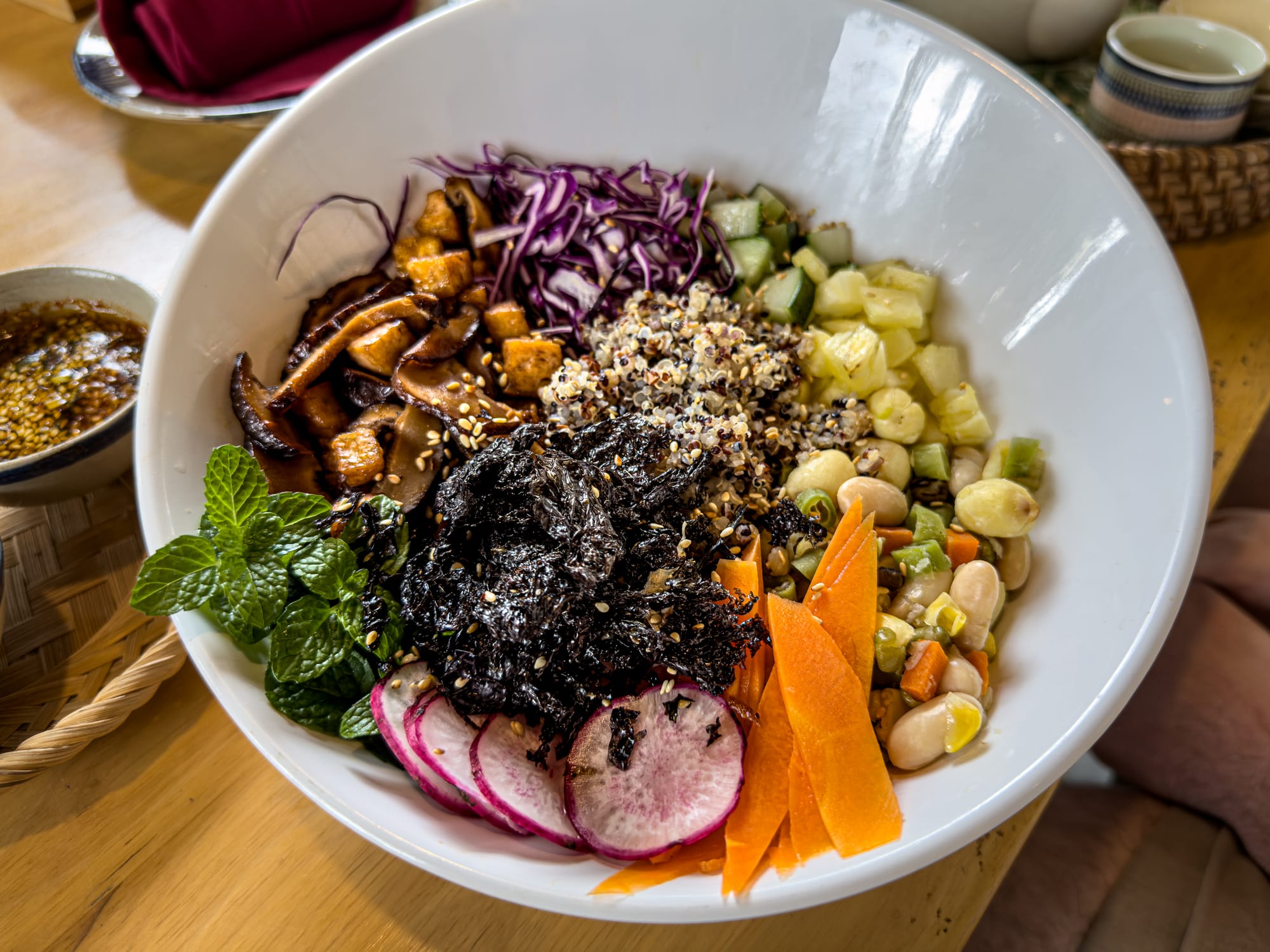 Vegan poke bowl at Rau Ơi Eatery in Hội An with tofu, shiitake mushrooms, quinoa, beans, cucumber, purple cabbage, radish, carrot, seaweed, and fresh mint, served with sesame soy dressing on the side