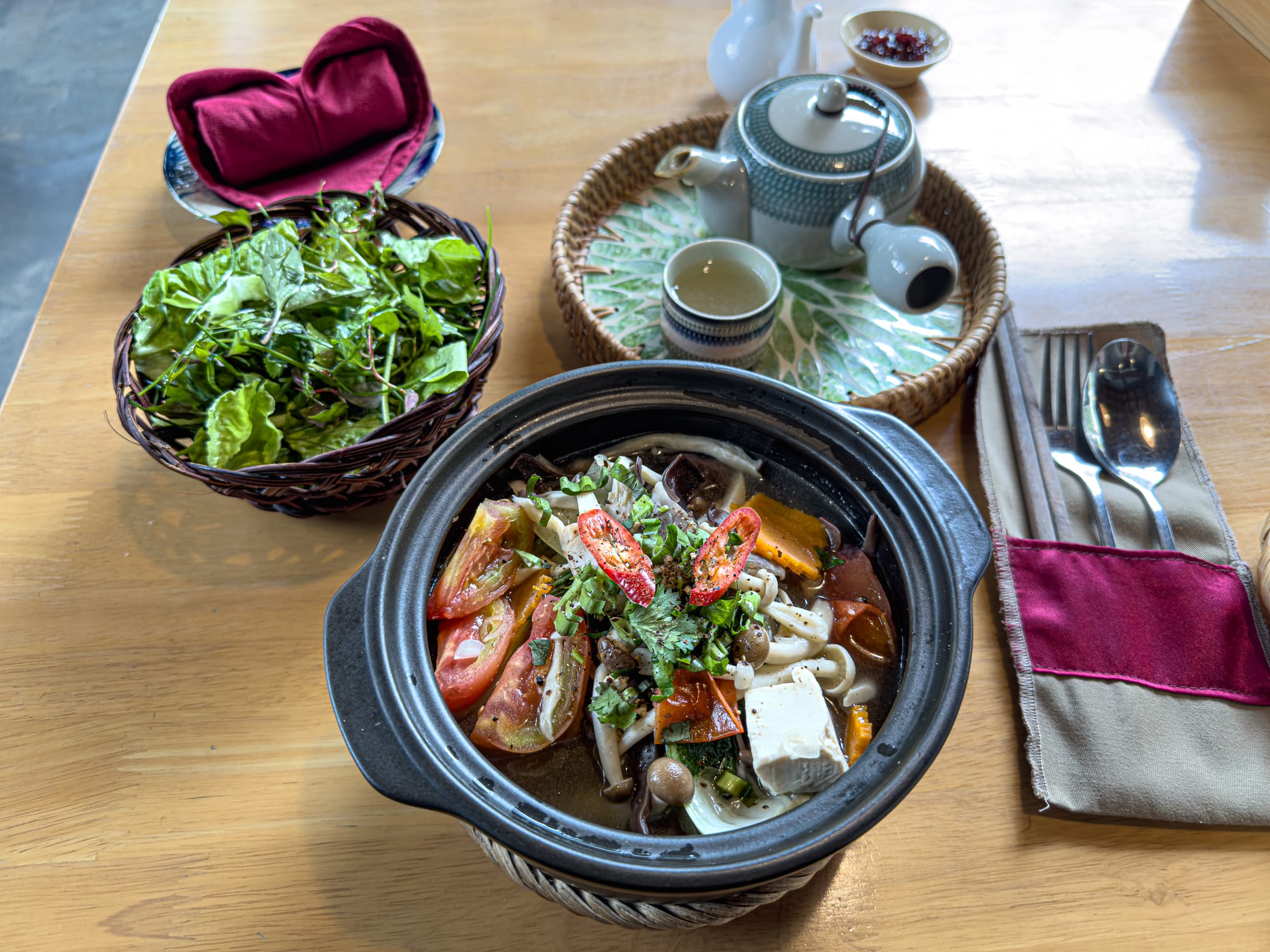 Vegan vermicelli soup at Rau Ơi Eatery in Hội An with tofu, mushrooms, tomatoes, chili, fresh herbs, and leafy greens on the side, served alongside hot tea