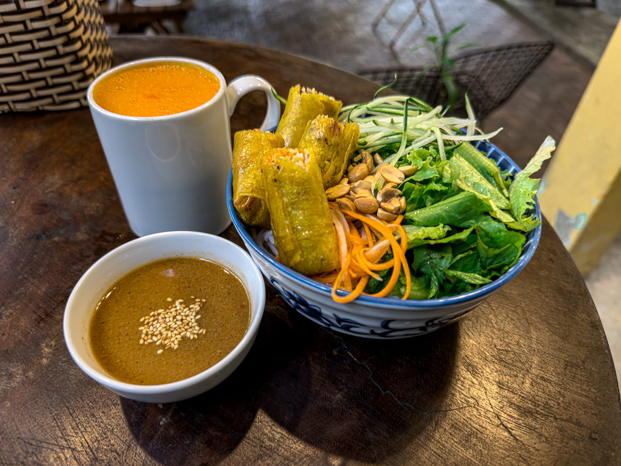 Vegan vermicelli salad at Chickpea Eatery in Hội An with fried spring rolls, fresh greens, shredded carrots, cucumber, peanuts, sesame dipping sauce, and a turmeric latte on the side