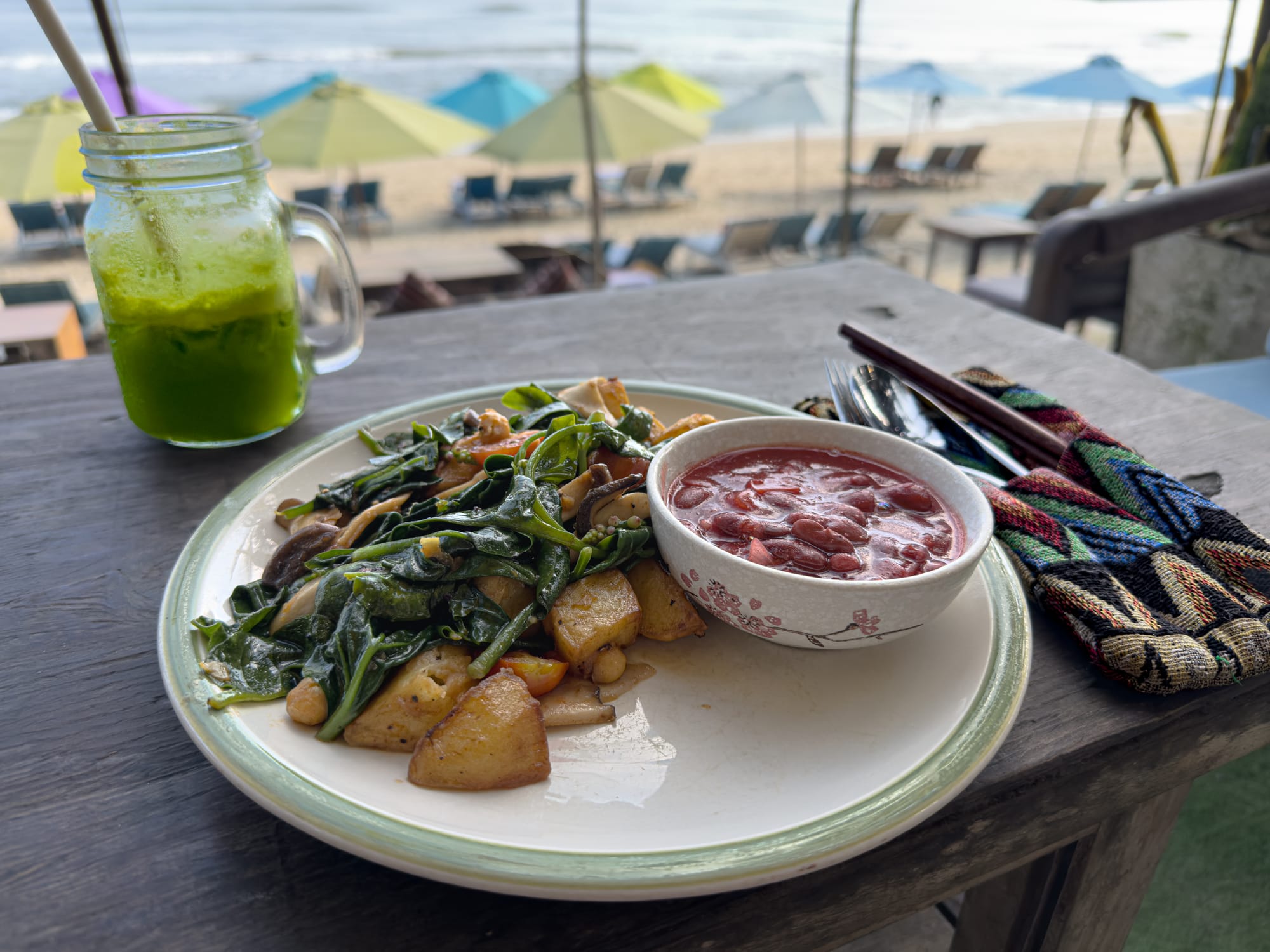 Vegan stir-fry with potatoes, leafy greens, and mushrooms served with red bean sauce and a fresh green juice at The Fisherman, a beachfront vegan restaurant on An Bàng Beach in Hội An