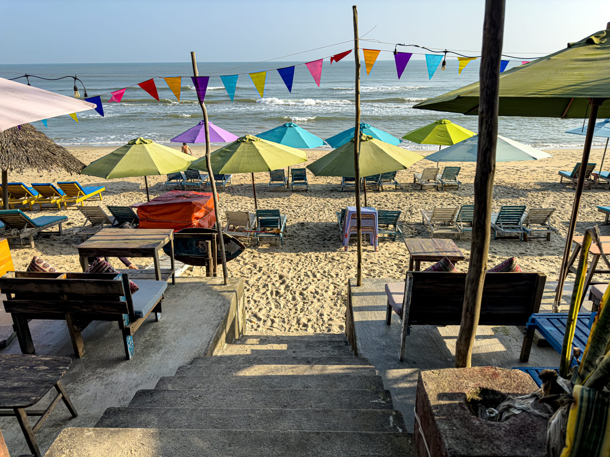 View from The Fisherman vegan restaurant at An Bàng Beach in Hội An, looking out over colorful umbrellas, beach chairs, and the ocean waves with bunting flags above