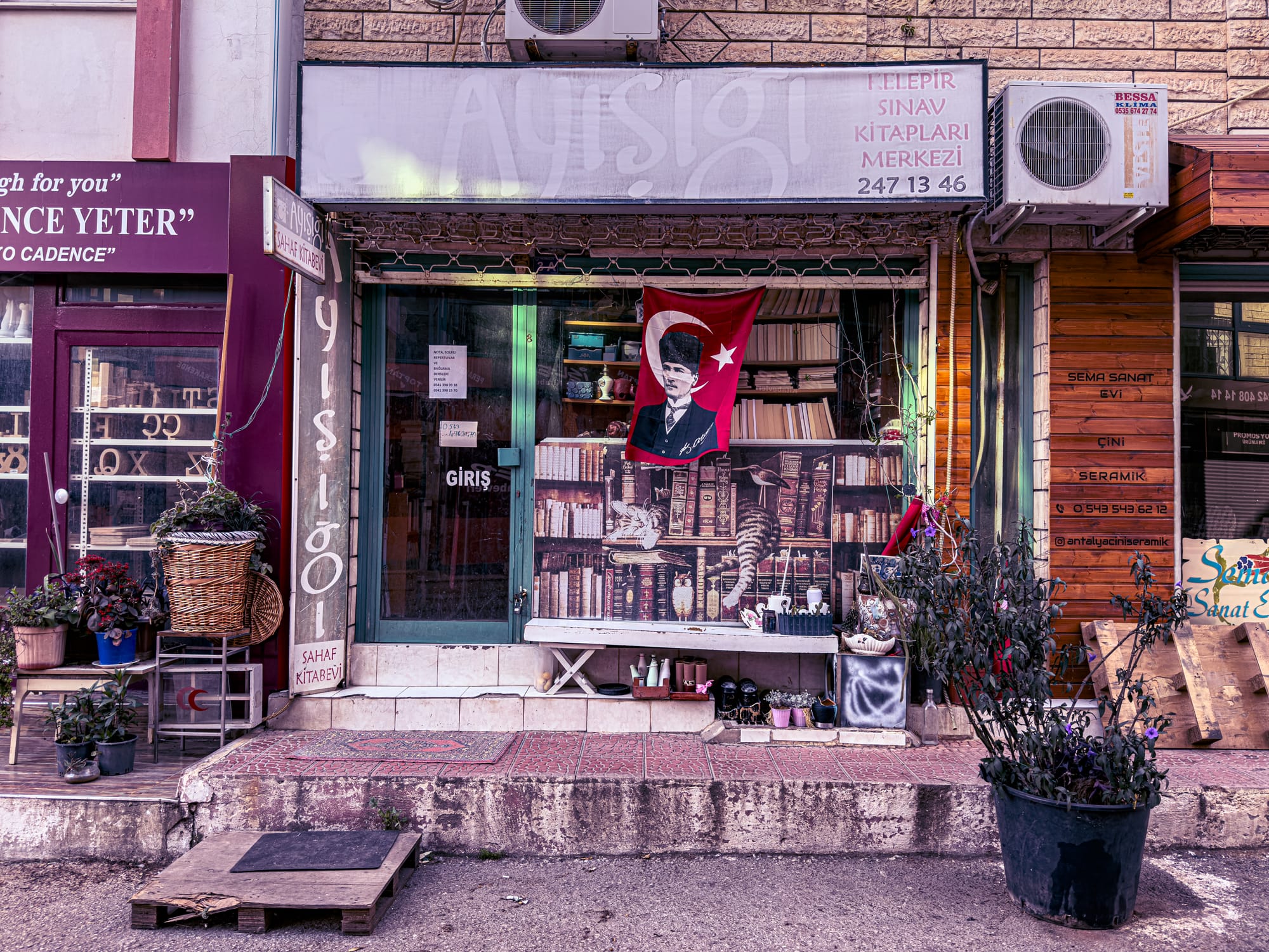 An eclectic local bookstore in Antalya with a Turkish flag, a mural of books, and potted plants lining the entrance