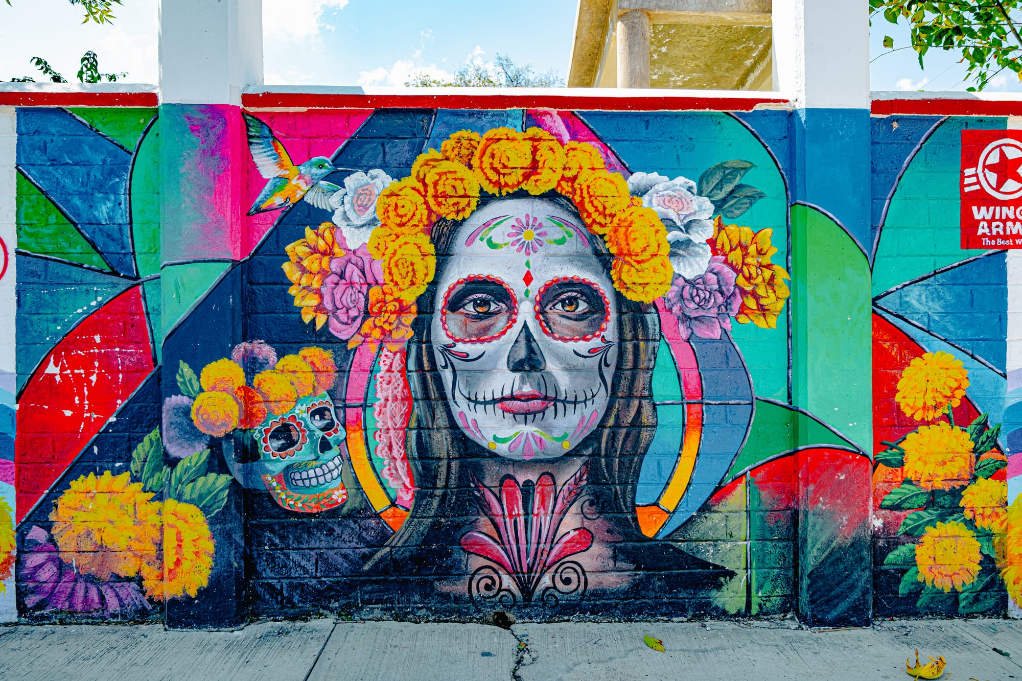 A colorful mural in San Cristóbal de las Casas depicting La Catrina with marigold and rose crowns, surrounded by bright flowers and a painted sugar skull, symbolizing the beauty and reverence of Mexico’s Day of the Dead tradition