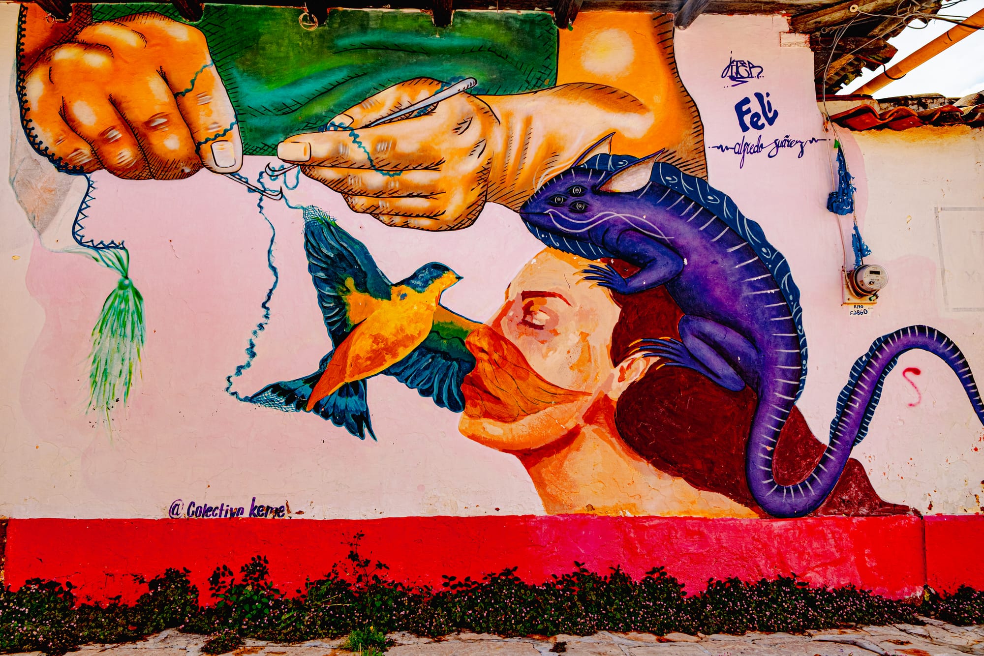 A mural in El Cerrillo, San Cristóbal de las Casas, showing large hands embroidering a blue thread connected to a bird, a woman’s face, and a purple iguana resting on her head, symbolizing creativity, interconnection, and the fusion of nature and imagination in Chiapas street art