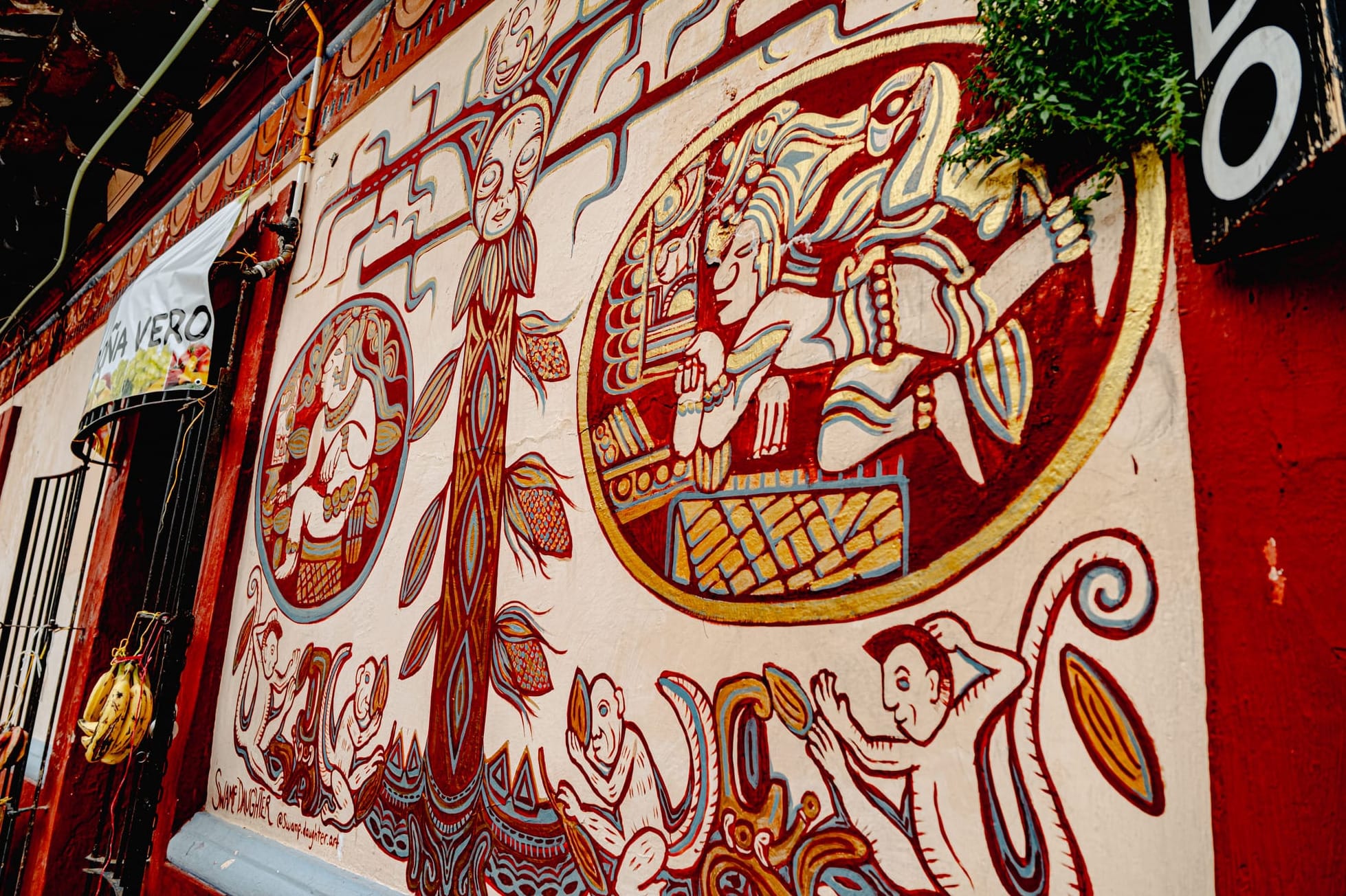 A detailed mural in El Cerrillo, San Cristóbal de las Casas, featuring Mayan-style figures, a central corn tree, and symbolic scenes of creation painted in earthy reds and golds, blending Indigenous cosmology with contemporary Chiapas artistry