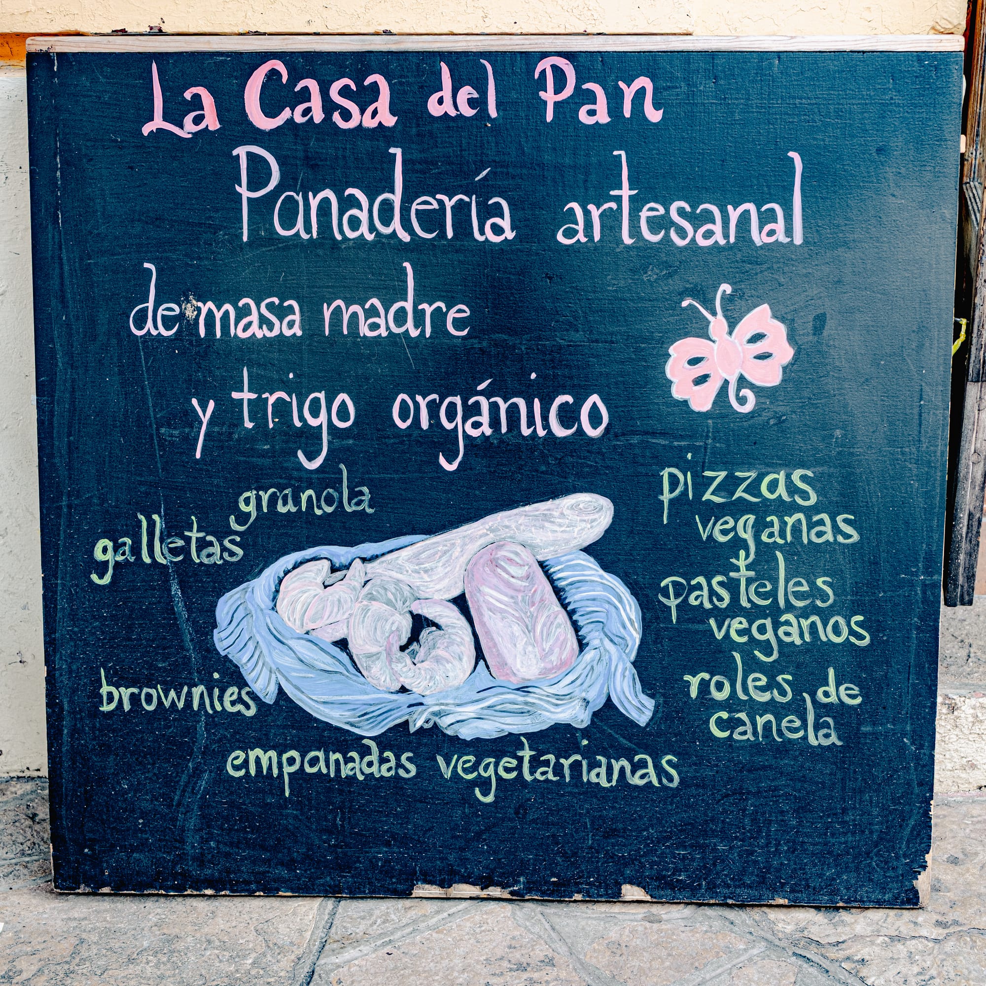A chalkboard sign at Casa del Pan in San Cristóbal de las Casas listing sourdough bread, organic wheat products, and several vegan items including pizzas, pastries, brownies, and empanadas