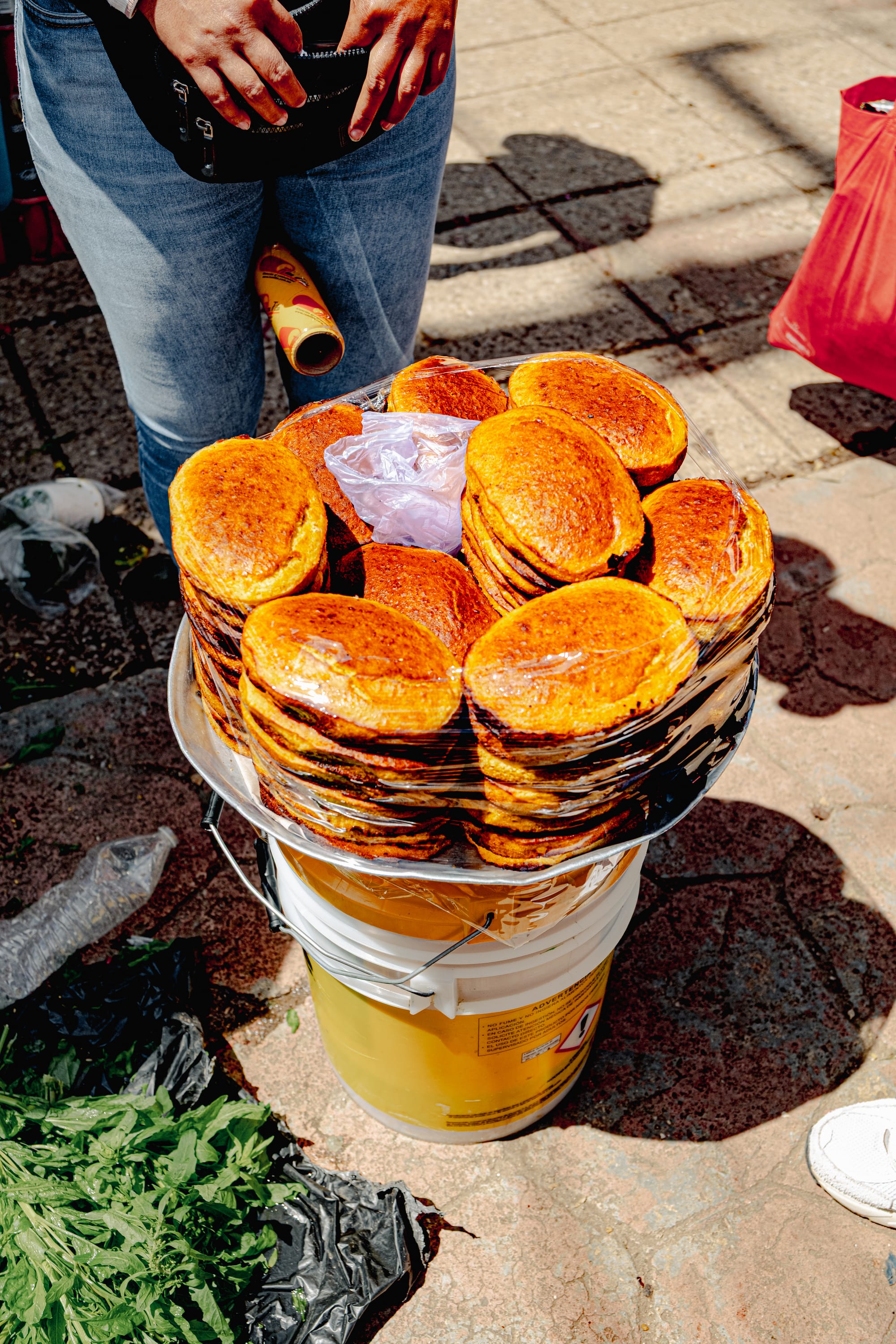 Close-up of freshly baked vegan cornbread rounds stacked and wrapped in plastic on a vendor’s tray at Santo Domingo Market in San Cristóbal de las Casas, Chiapas