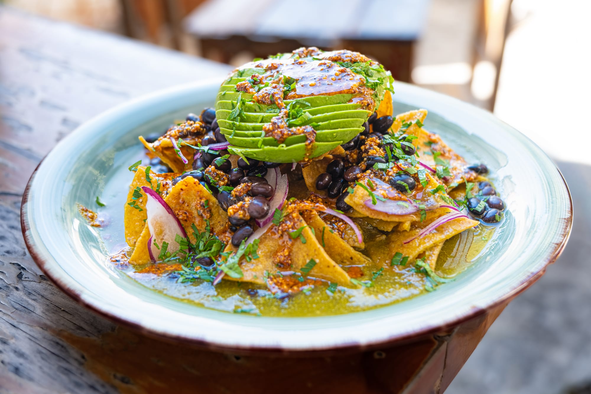 A plate of vegan chilaquiles from Astro Café in San Cristóbal de las Casas, topped with sliced avocado, black beans, red onion, cilantro, and salsa verde