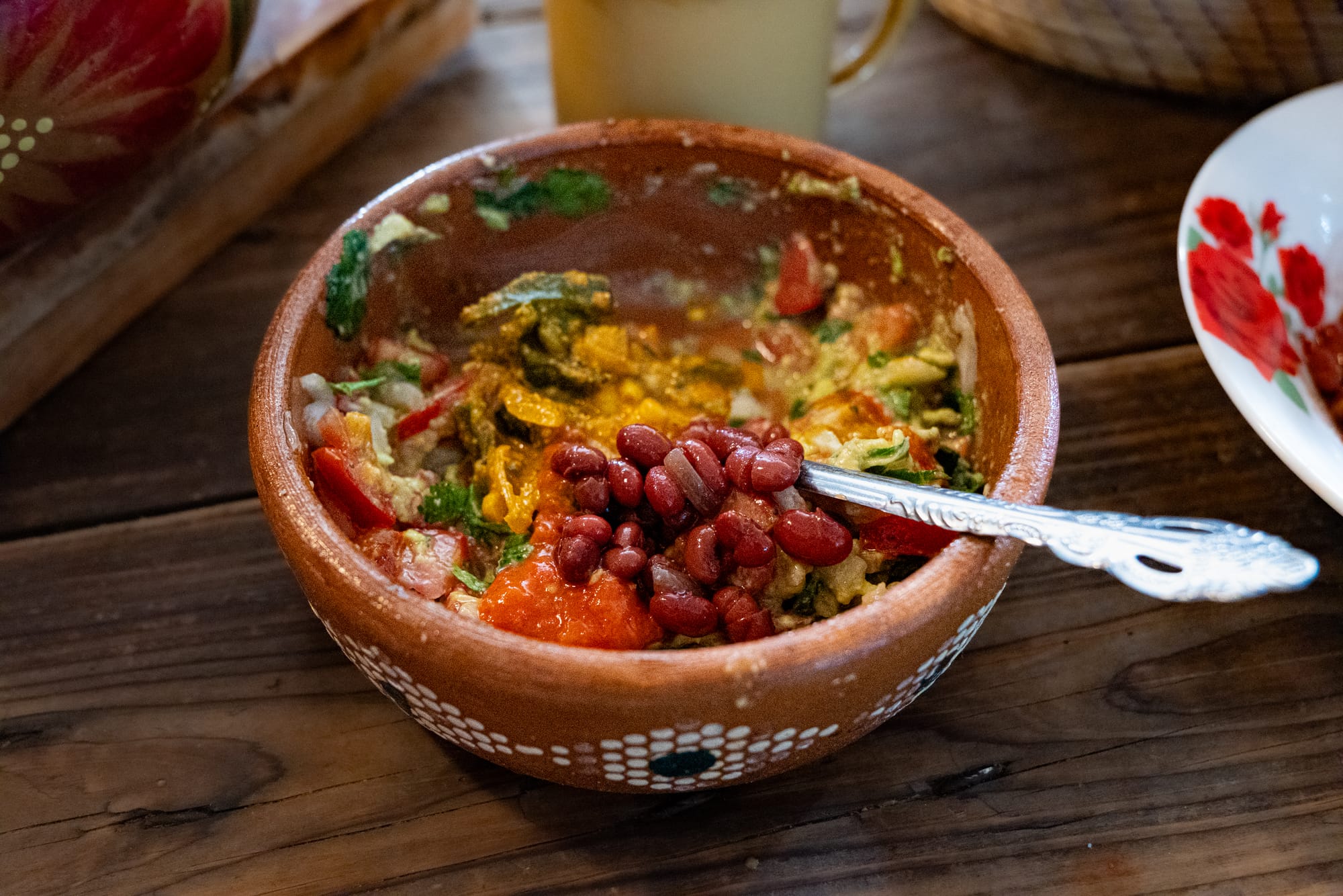 A bowl of vegan rajas con queso with tomatoes, greens, and red beans at Art Libreria in San Cristóbal de las Casas, served in a traditional clay dish