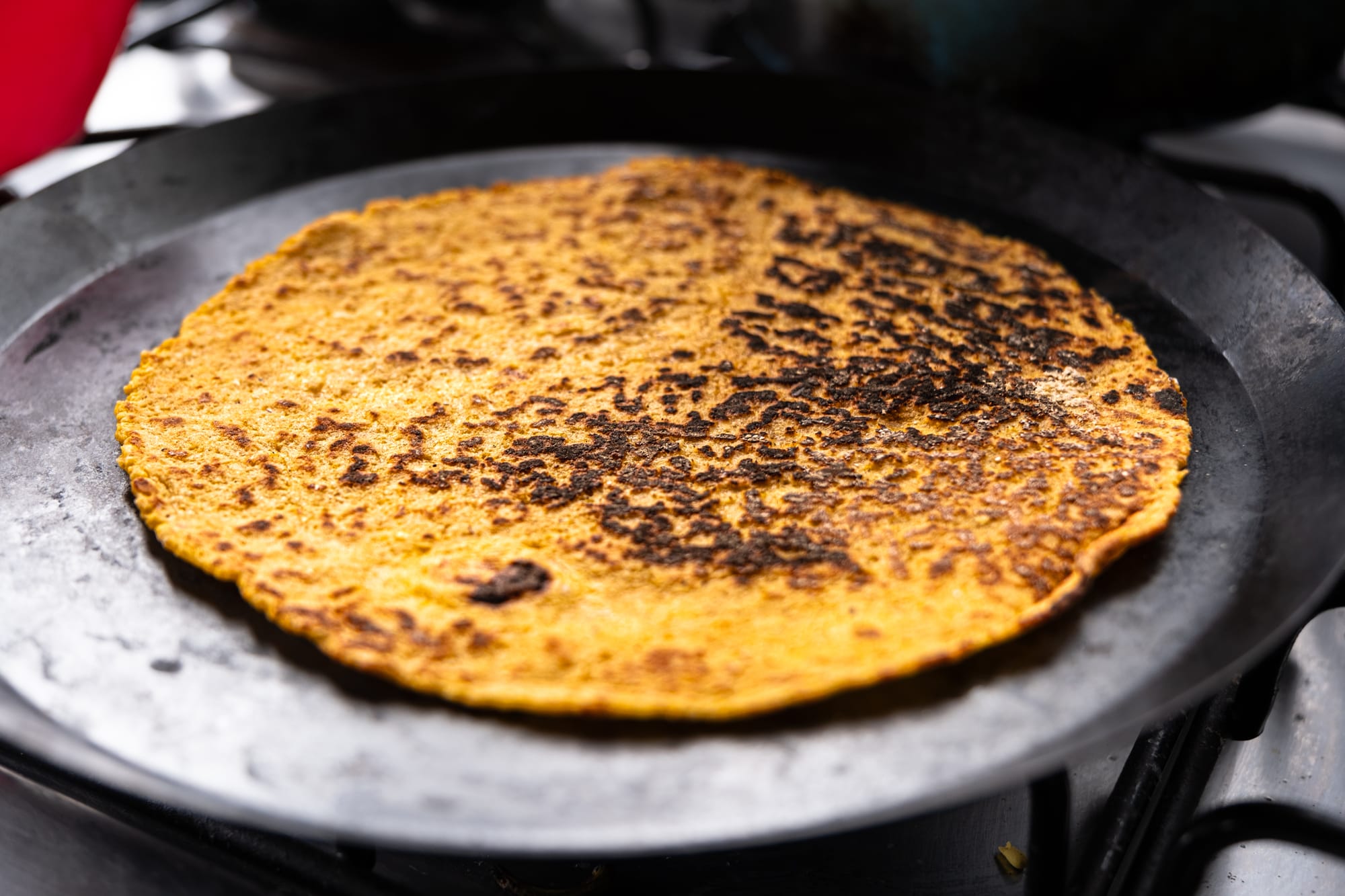 A close-up of a golden corn tortilla, its surface speckled with char